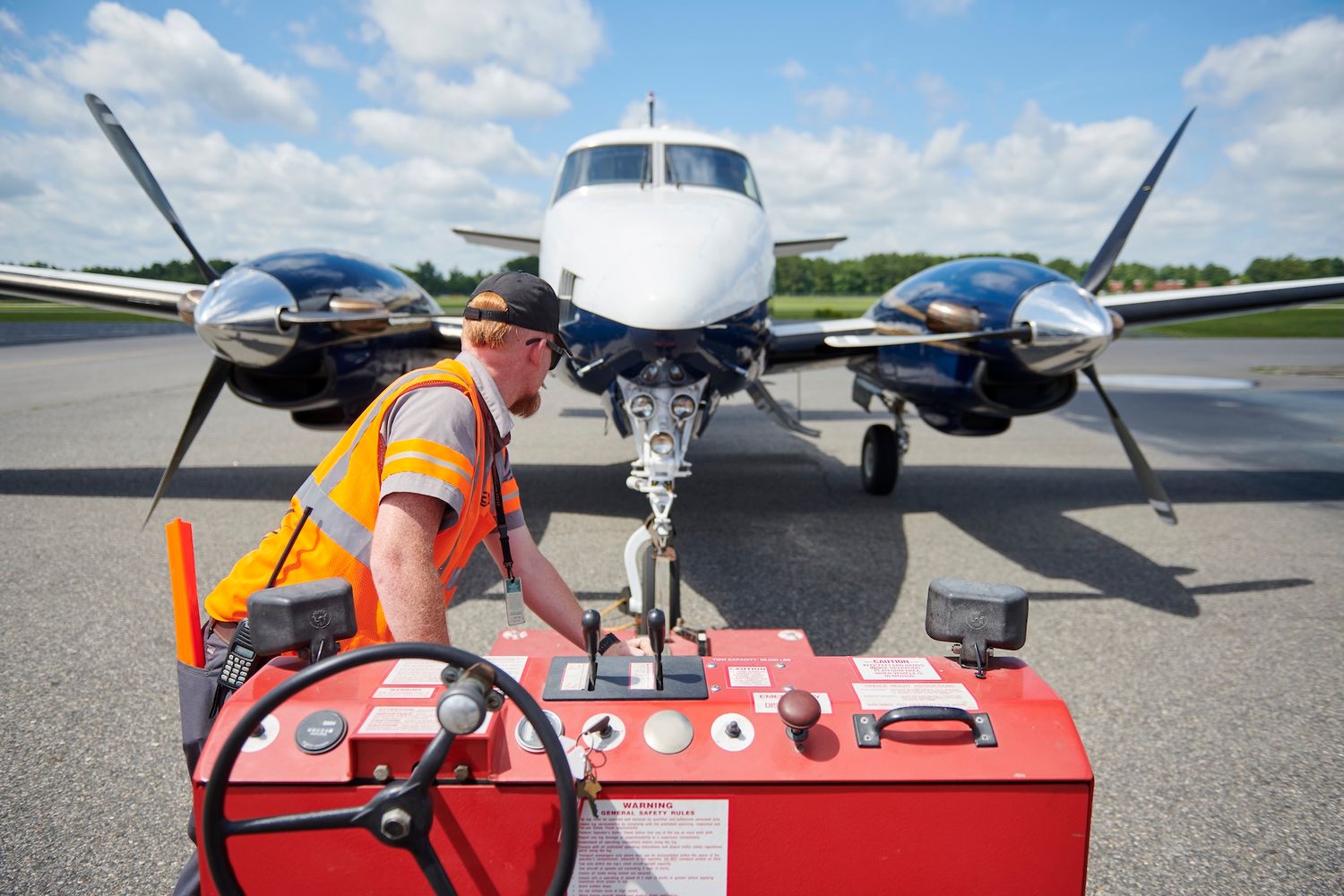 Airport ground crew worker fueling a twin-engine propeller aircraft on sunny tarmac runway.