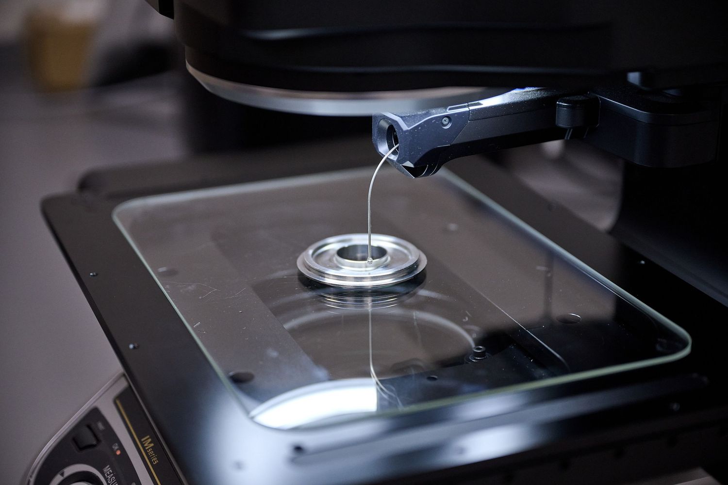 Close-up of a microscope lens dispensing liquid onto a glass slide in a laboratory setting.
