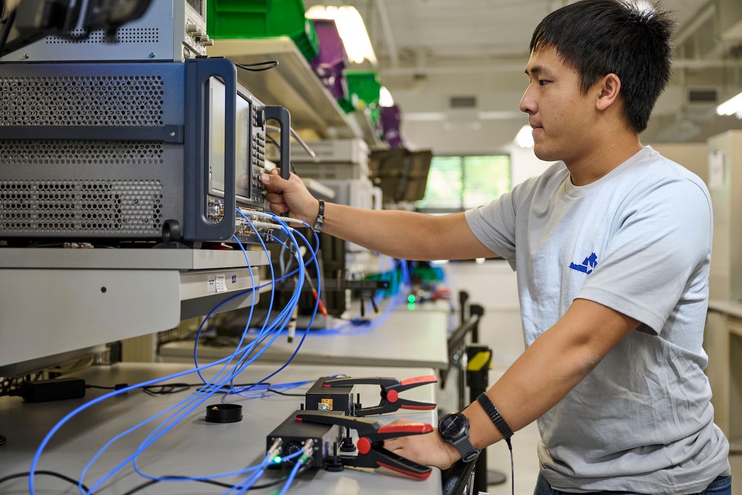 Asian engineer connecting blue cables to electronic testing equipment in technology lab.