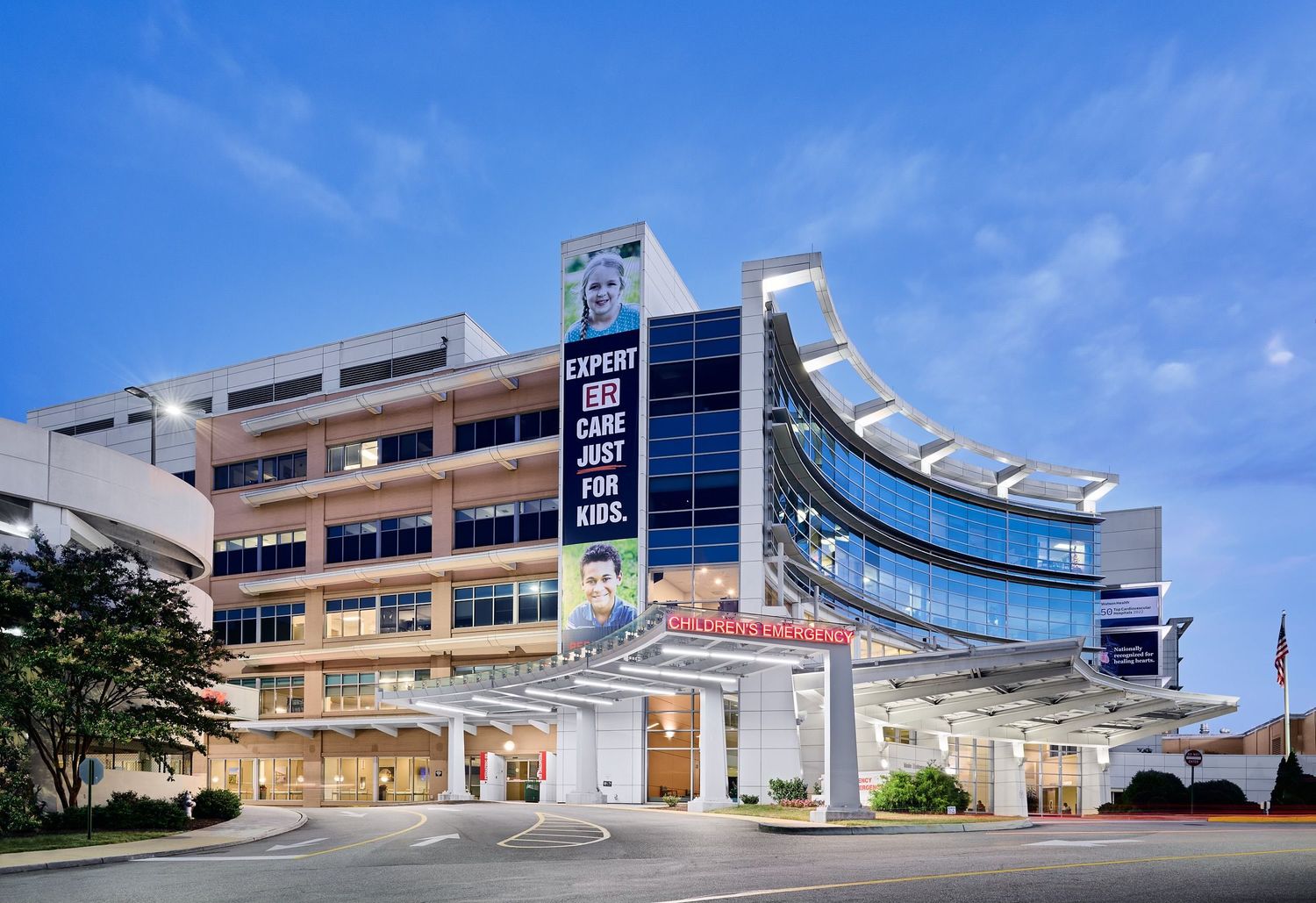 Childrens hospital exterior at dusk with Expert Care Just For Kids signage illuminated.