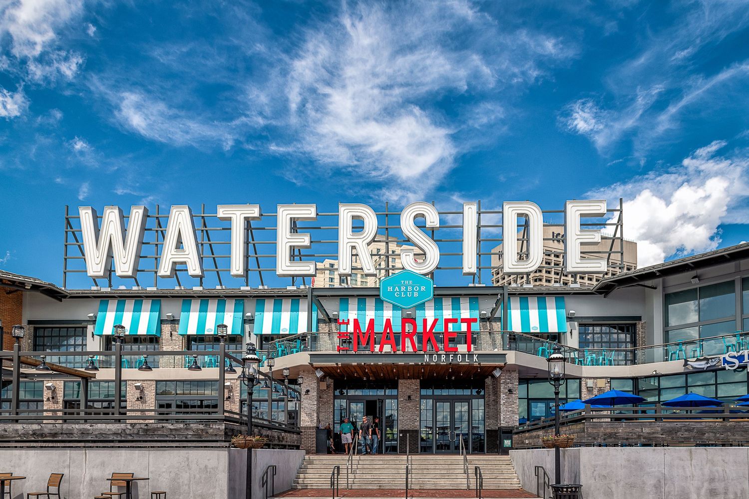 Waterside Market sign above a bustling waterfront marketplace under a blue sky.