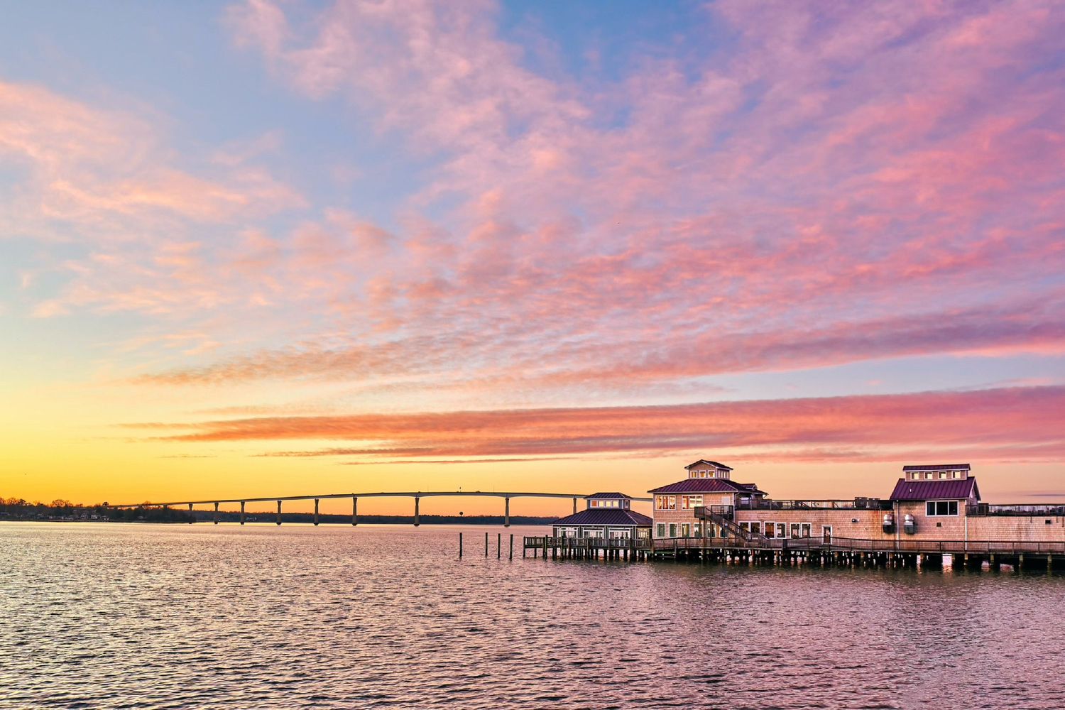 Stunning waterfront pier and pavilion at sunset with vibrant pink and orange sky reflecting on calm water.