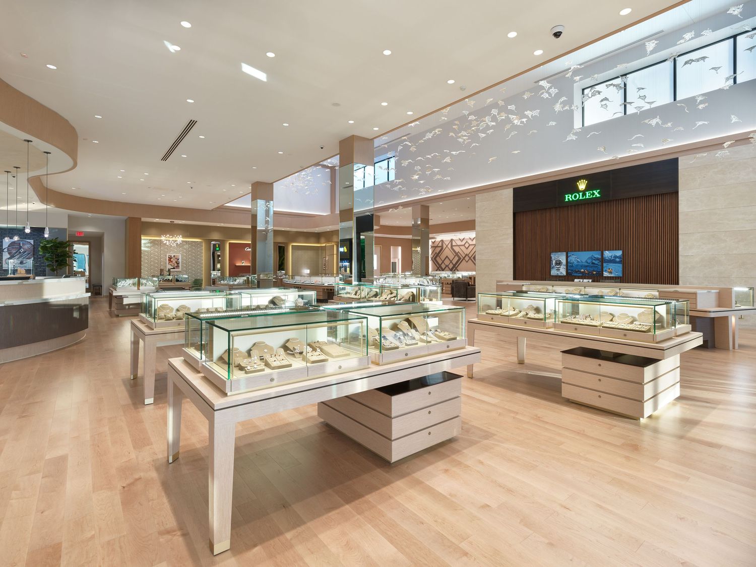 Luxury jewelry showroom with glass display cases, wood floors, and Rolex branded section.