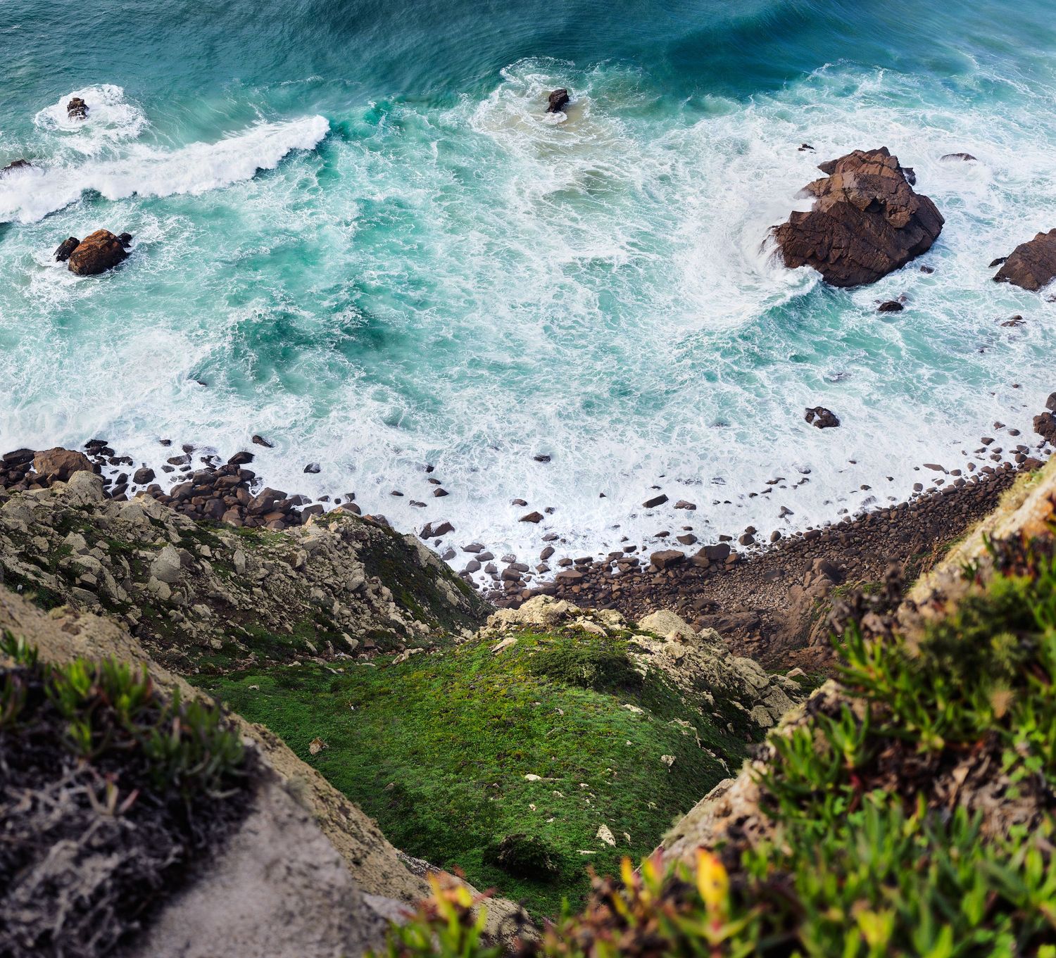 Aerial view of turquoise ocean waves crashing against rocky coastal cliffs.