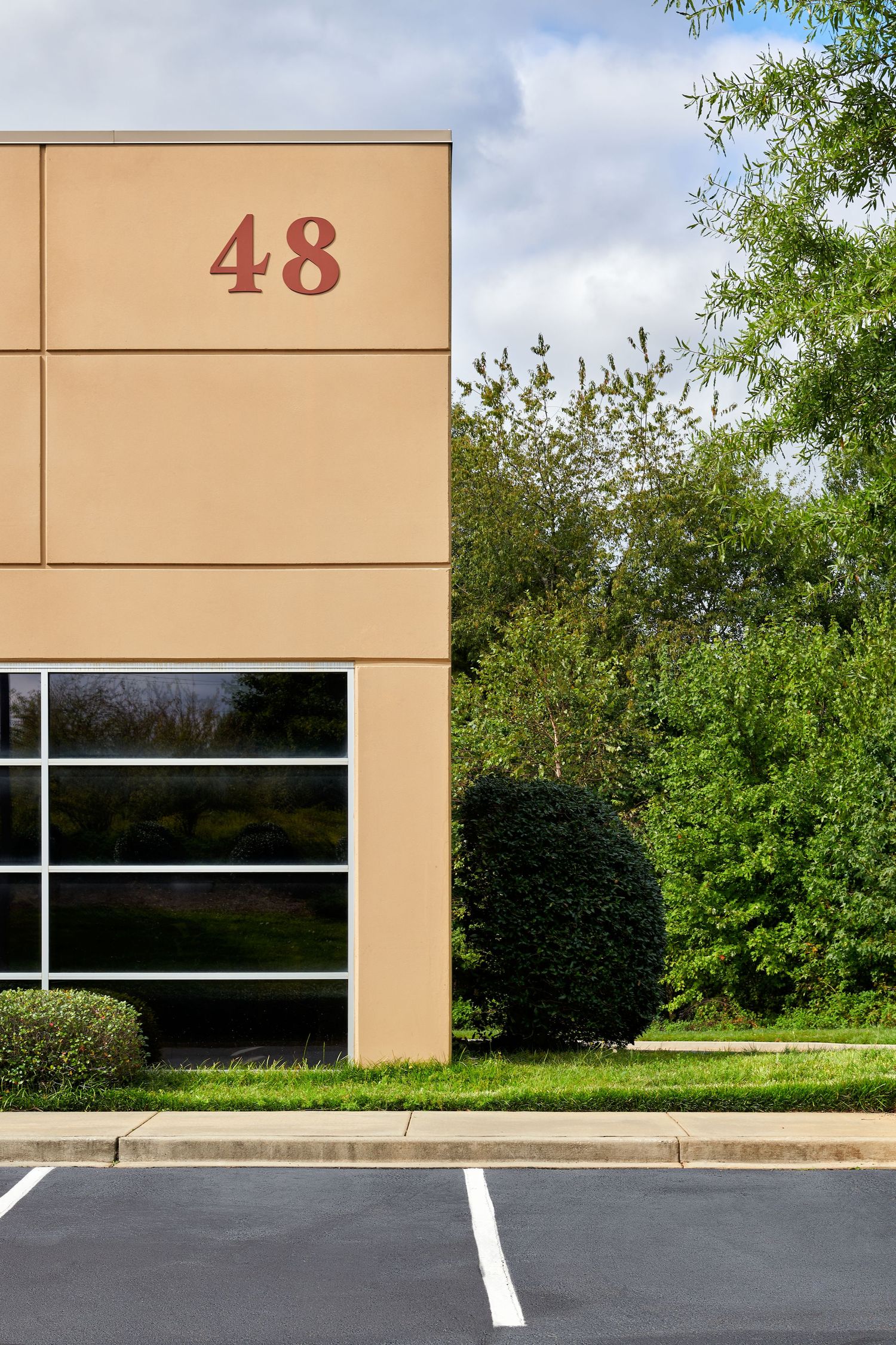 Exterior of commercial building number 48 with tan facade, glass windows, and surrounding green trees.