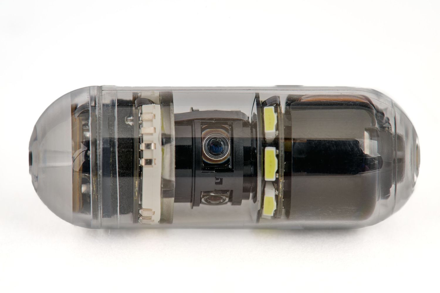 Transparent capsule endoscopy medical device with camera and LED lights on white background.