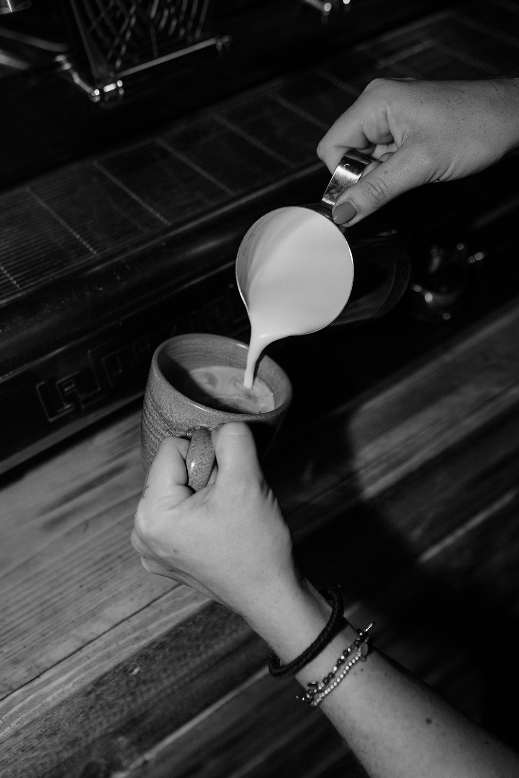 Barista pouring steamed milk into a rustic ceramic coffee cup in black and white.