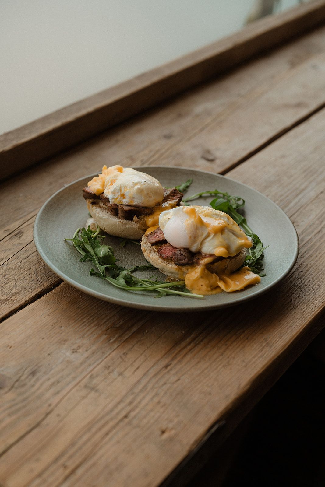 Two eggs Benedict with hollandaise sauce on English muffins, served with fresh arugula on a rustic wooden table.