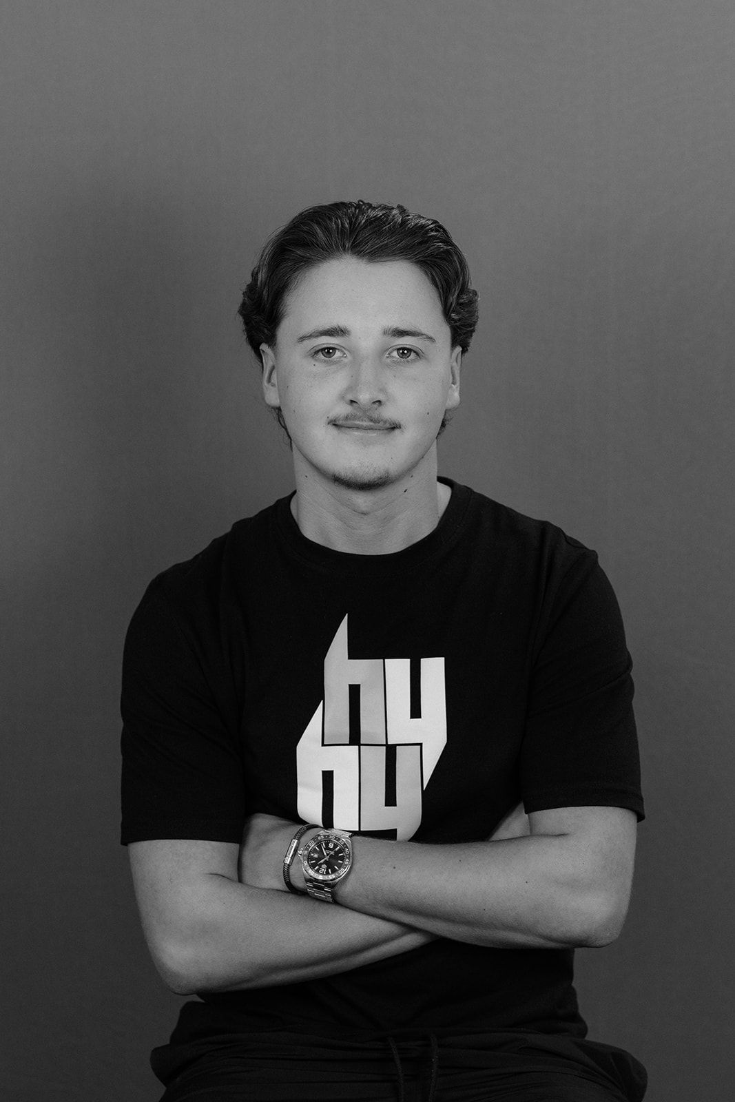 Young man with crossed arms wearing a black graphic t-shirt and watch, posing for a professional portrait photo.
