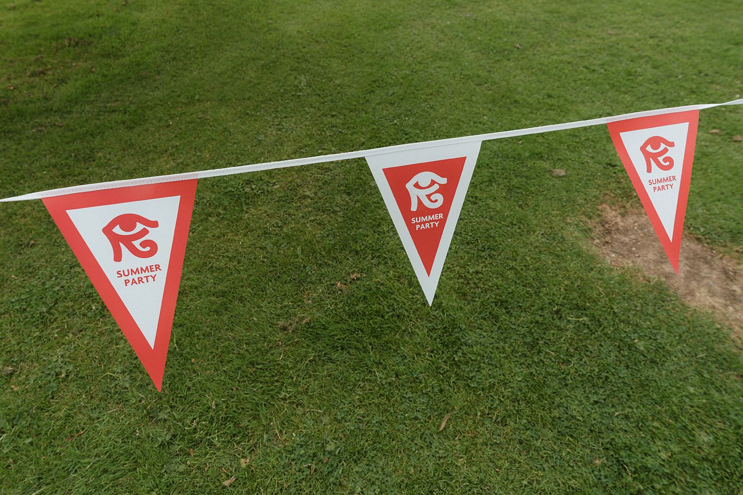 Red and white triangular Summer Party bunting flags displayed on a green grass lawn.