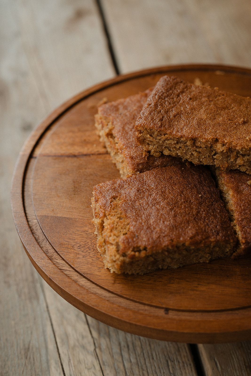 Stack of golden-brown blondies or cornbread squares on a round wooden cutting board.