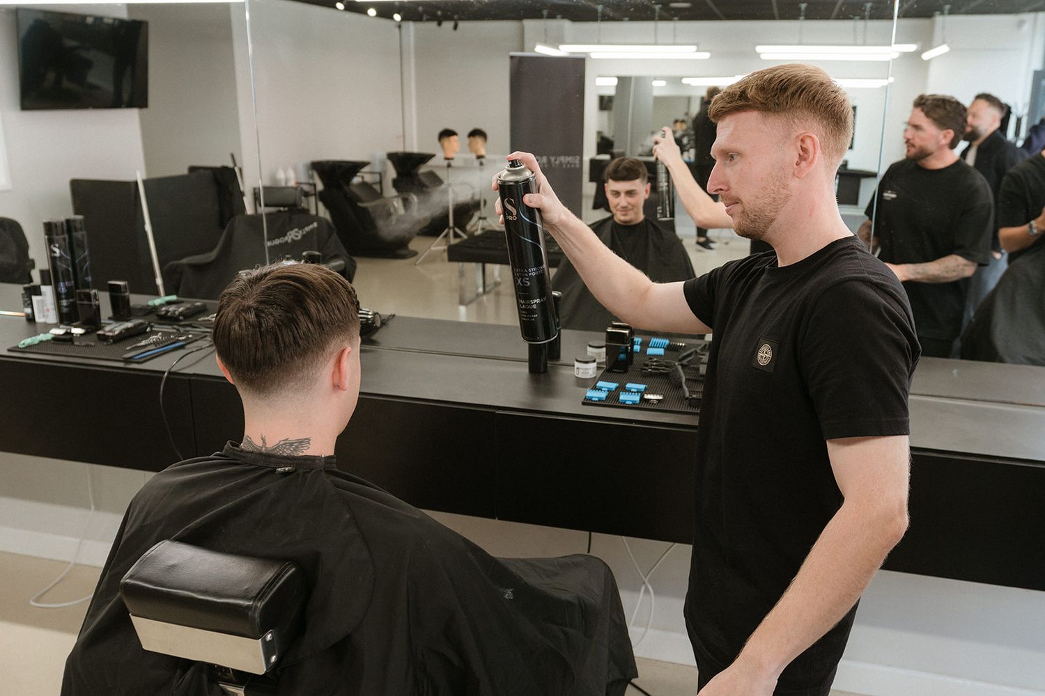 Barber styling a male client's hair with a spray bottle in a contemporary barbershop.