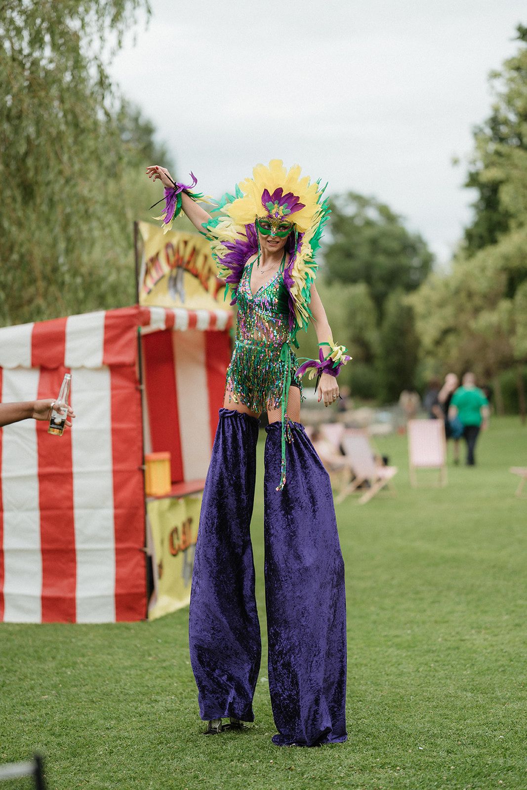 Colorful carnival stilt walker in feathered costume and mask performing at an outdoor summer festival event.