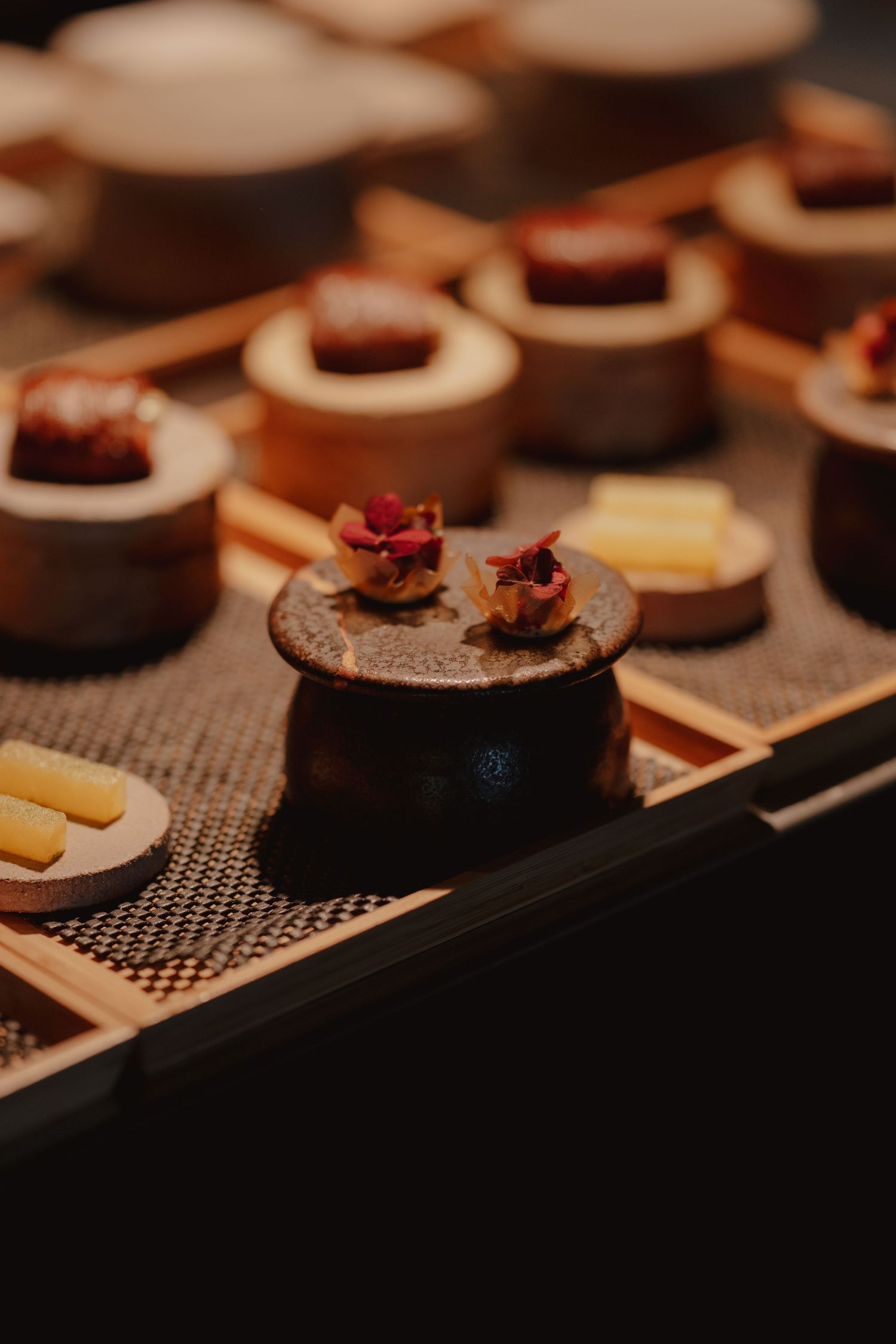 Elegant Japanese omakase appetizers served on wooden pedestals with edible flowers at a fine dining restaurant.