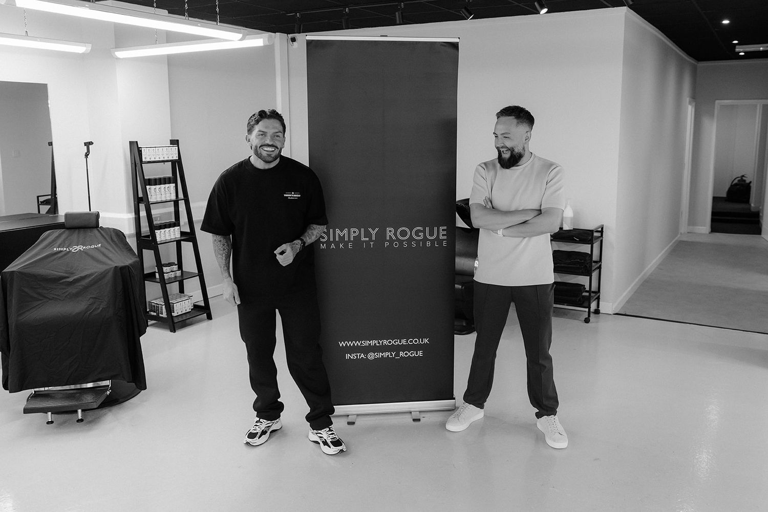 Two men stand beside a Simply Rogue branded pull-up banner in a modern white studio space.