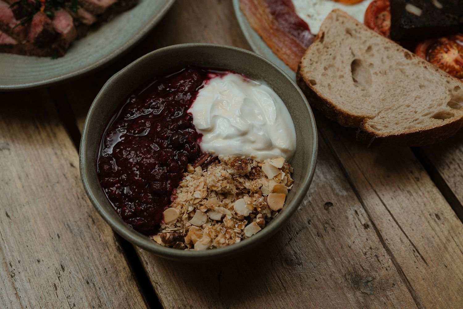 Ceramic bowl of berry compote topped with granola and yogurt on a rustic wooden table.