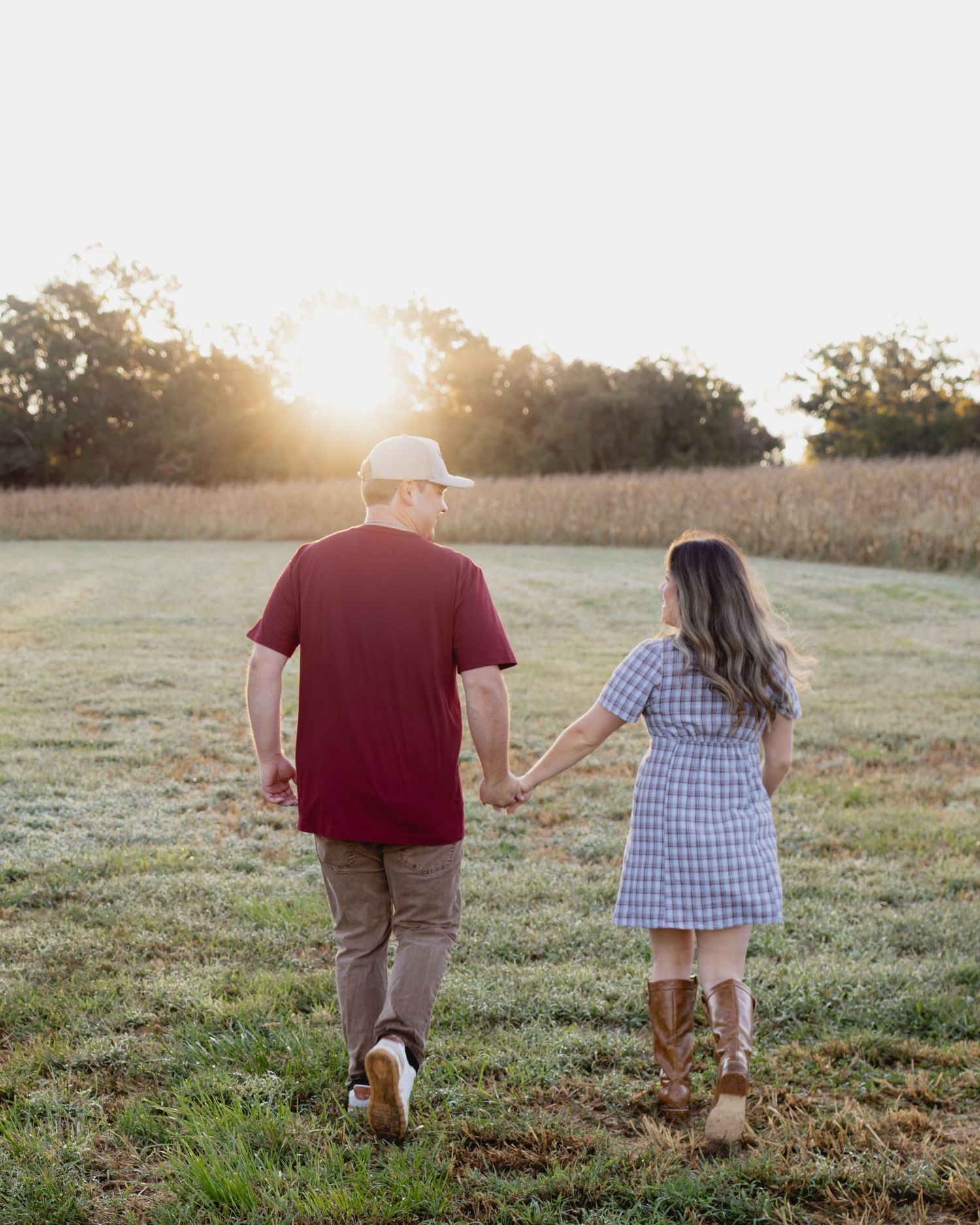 A man in a red shirt and hat holds hands with a young girl in a blue dress walking through a sunny field.