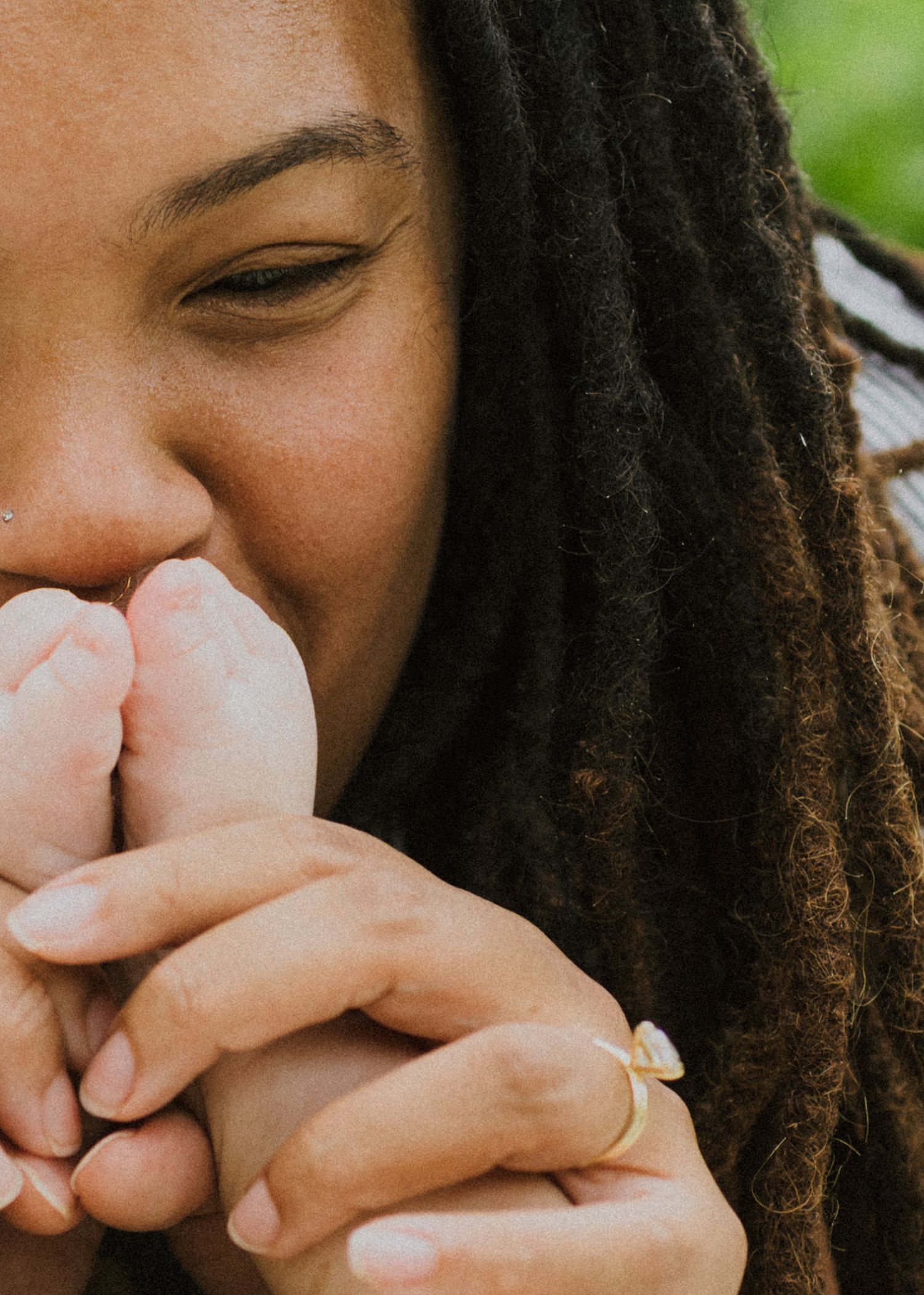 Woman with dreadlocks tenderly kissing a newborn baby's tiny feet up close.
