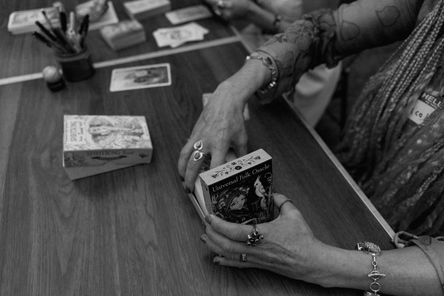 Elderly woman's hands holding tarot cards on wooden table in black and white photography.