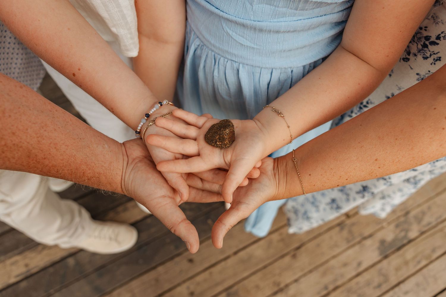 Three people stacking hands together on a wooden deck, wearing bracelets and watches, symbolizing unity and connection.