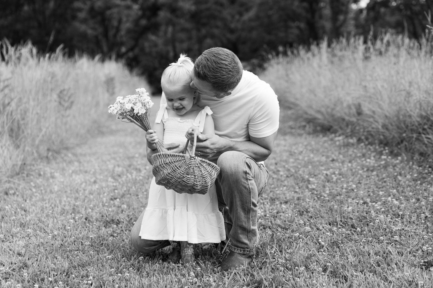 Black and white photo of a father kneeling beside his young daughter holding a flower basket.