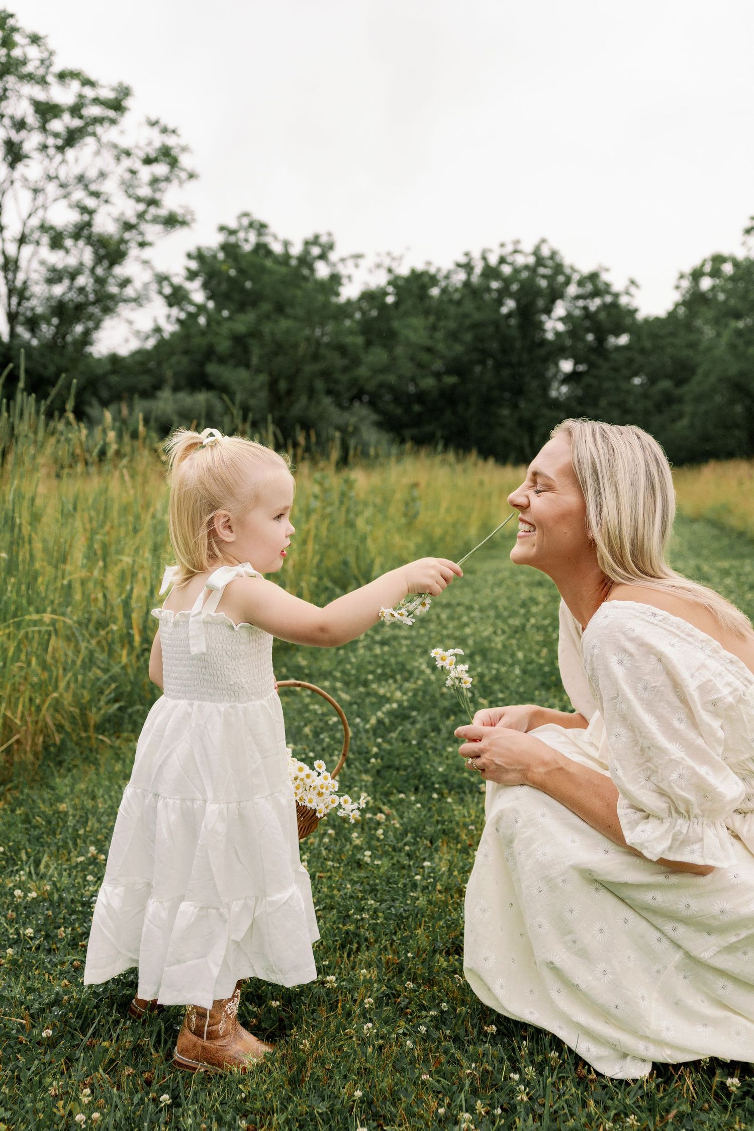 Toddler girl offers a flower to her smiling mother while sitting in a green meadow.