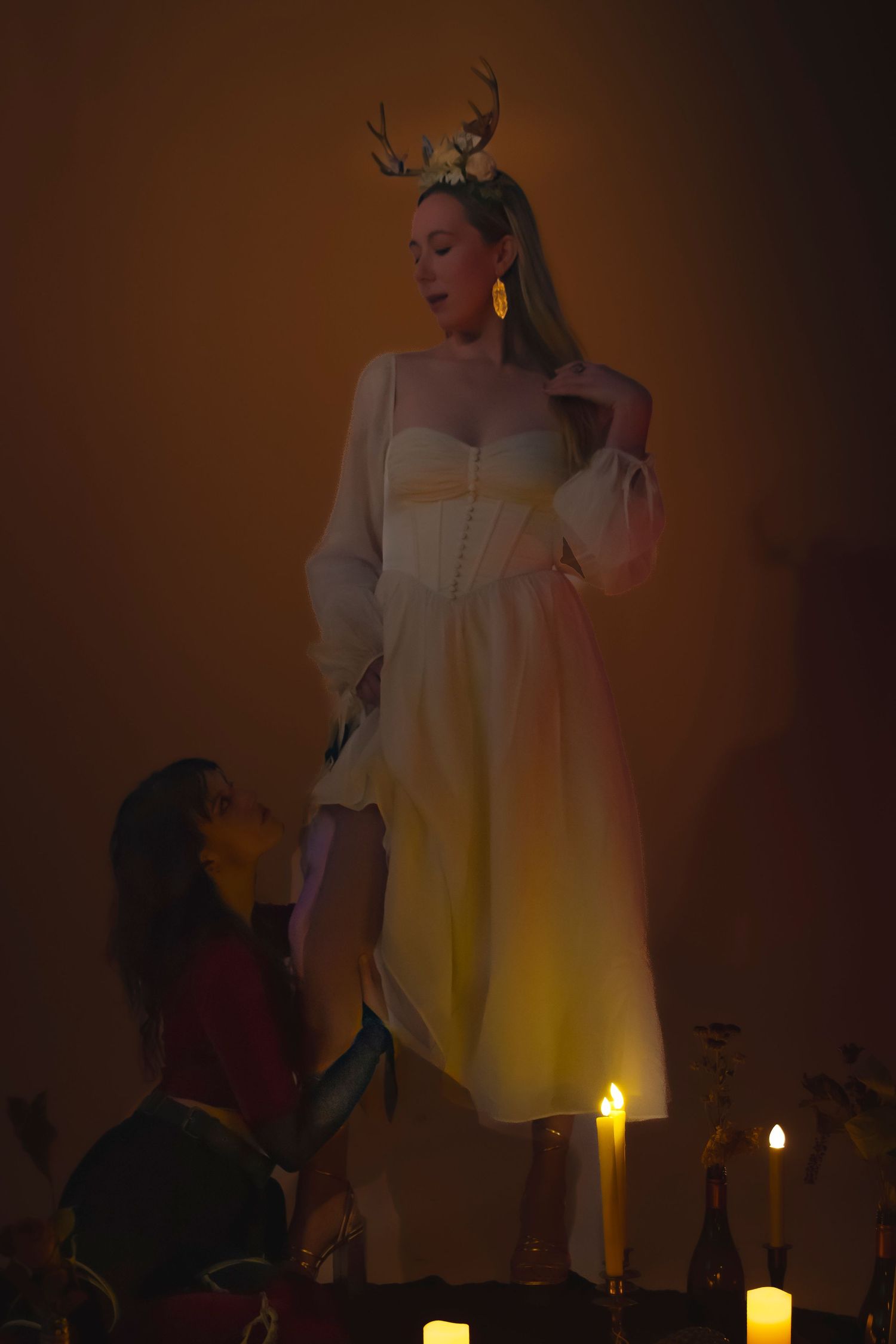 A theatrical performance lit by candlelight shows figures in period costumes against a warm amber background.