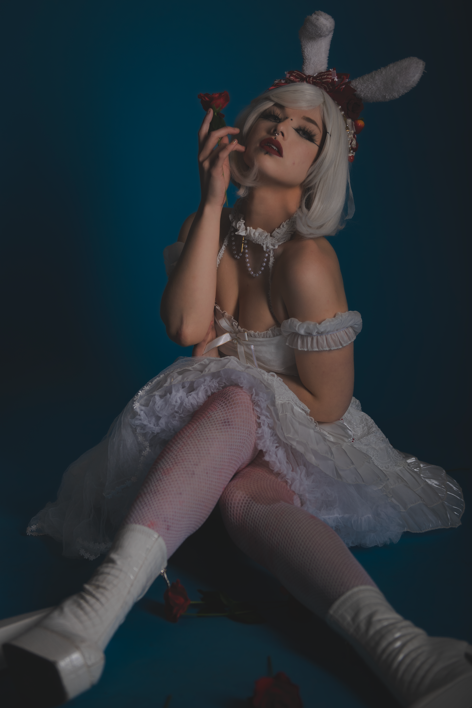 Artistic portrait showing white dress, boots and roses in moody blue lighting.