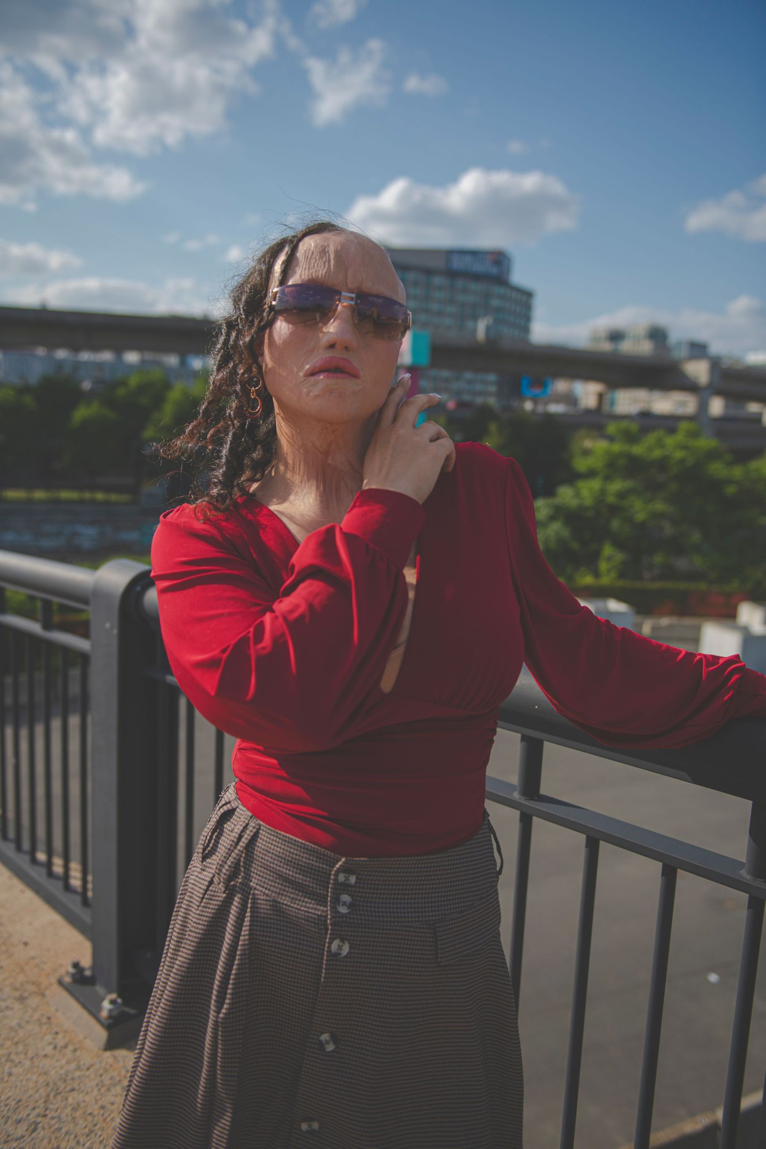 Urban fashion photo with sunglasses and red sweater against city backdrop on a sunny day with blue skies.