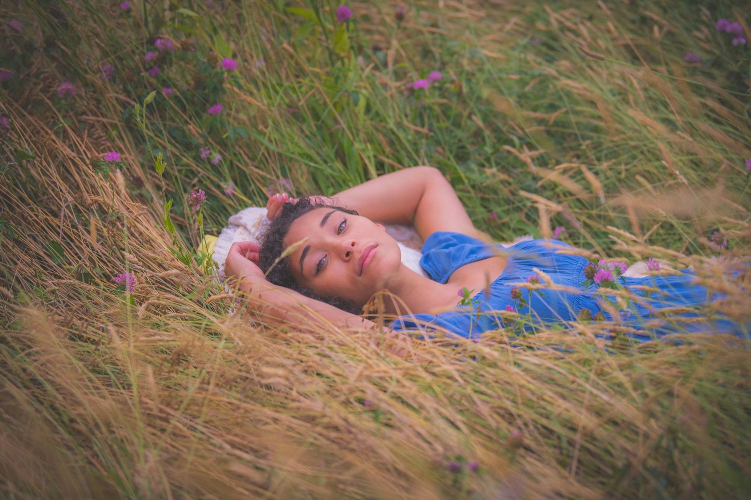 Woman in blue dress lying peacefully in tall golden grass.