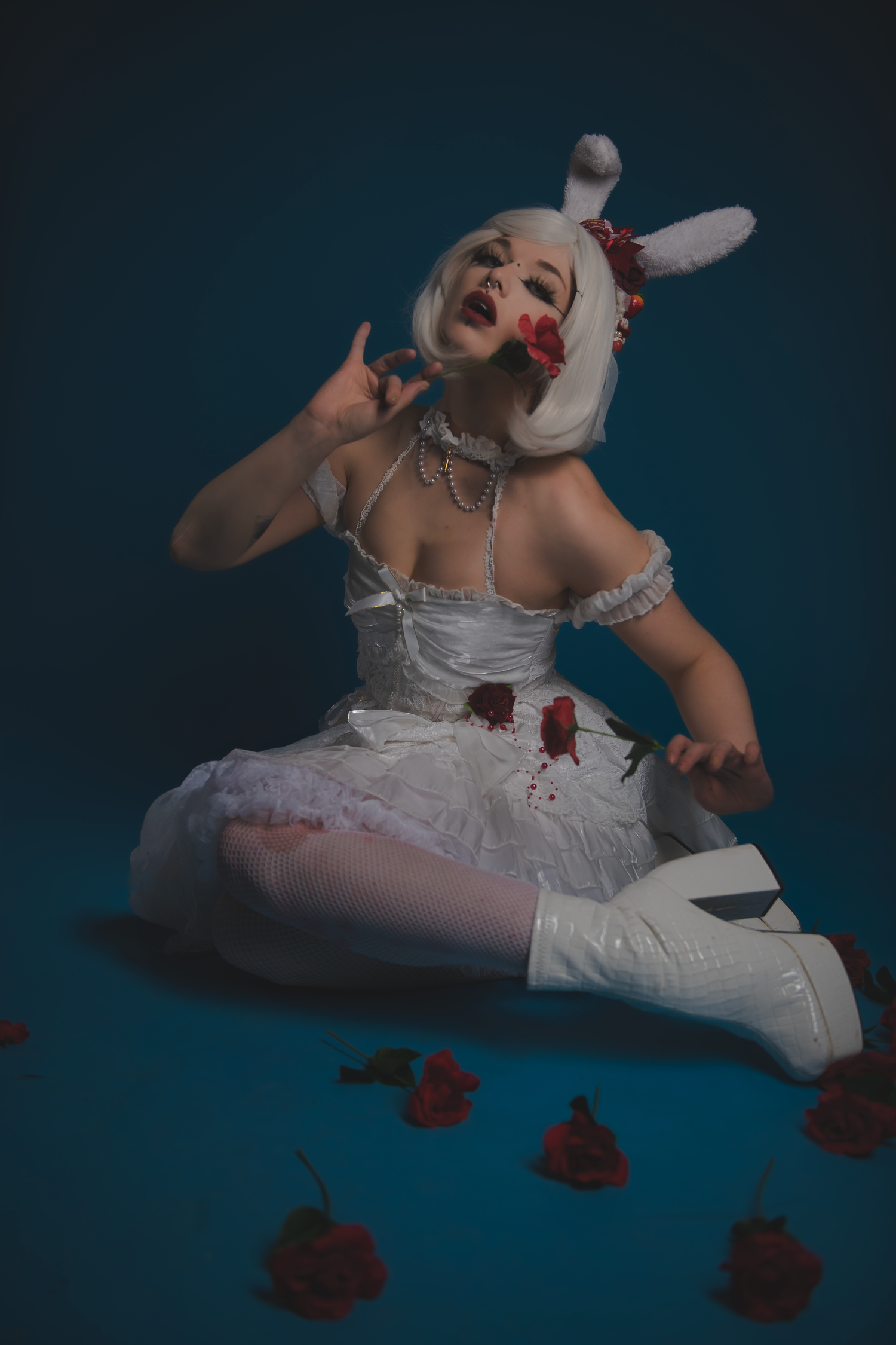 Theatrical scene with white costume and scattered red roses on floor.