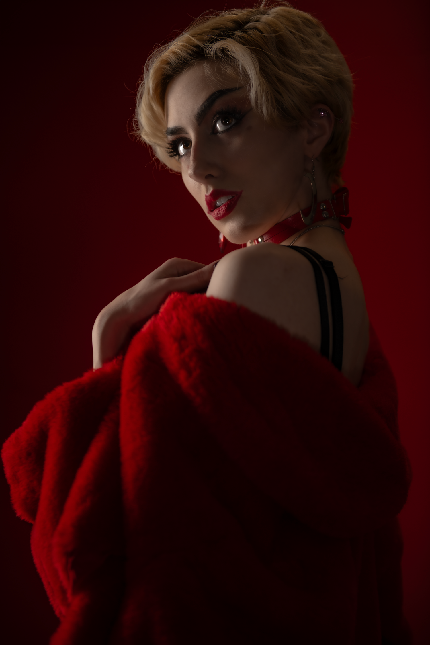Dramatic portrait against red background featuring blonde hair and red coat in vintage glamour style lighting.