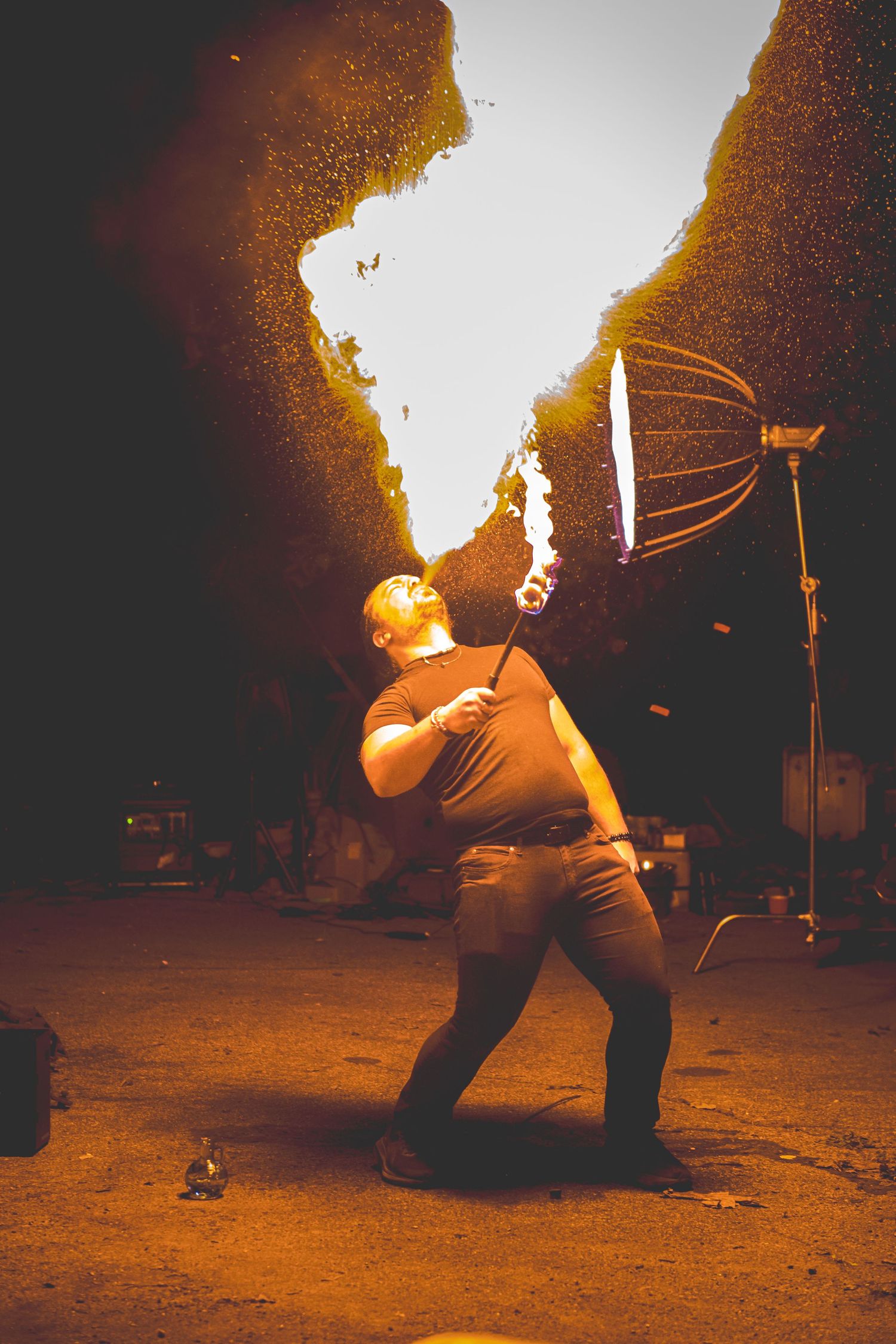 A person performing a fire breathing stunt at night, creating dramatic arcs of flame against a dark background.