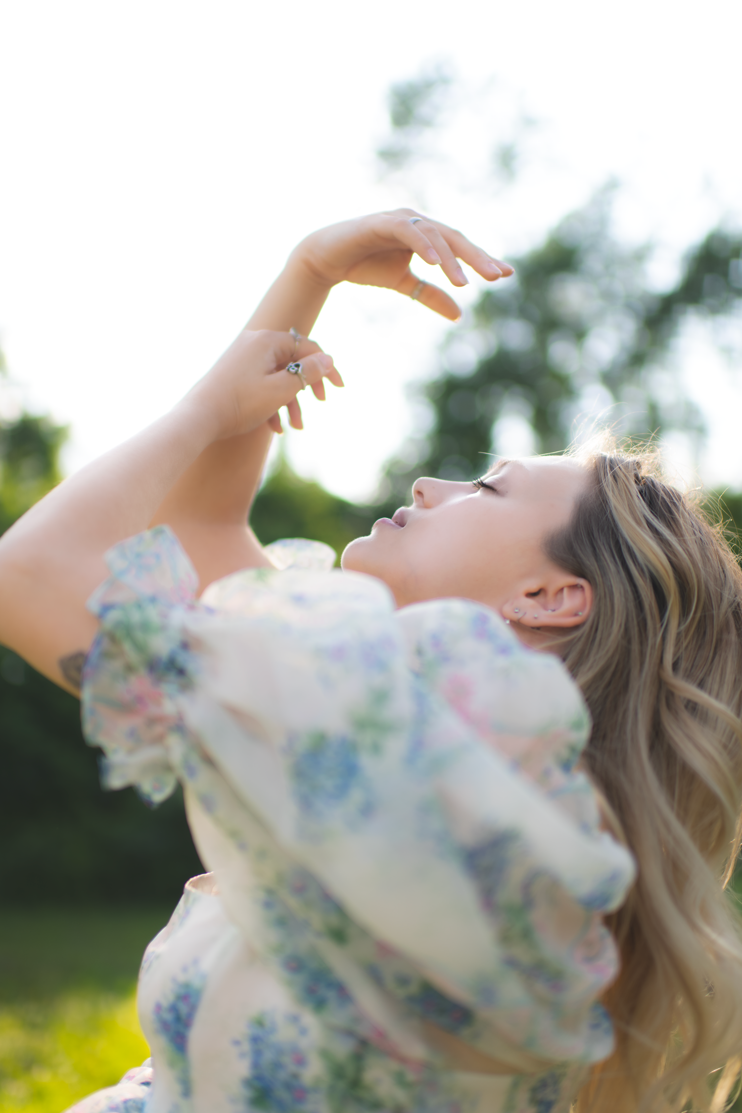 A dreamy portrait of someone in a floral dress twirling against a sunlit outdoor backdrop.