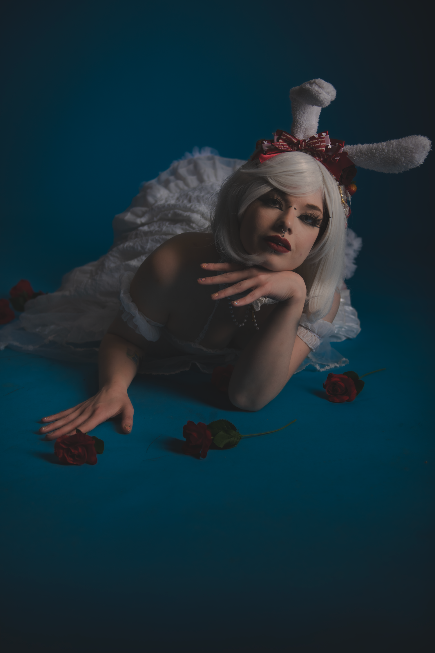 Artistic portrait in white dress with scattered rose petals against blue background.