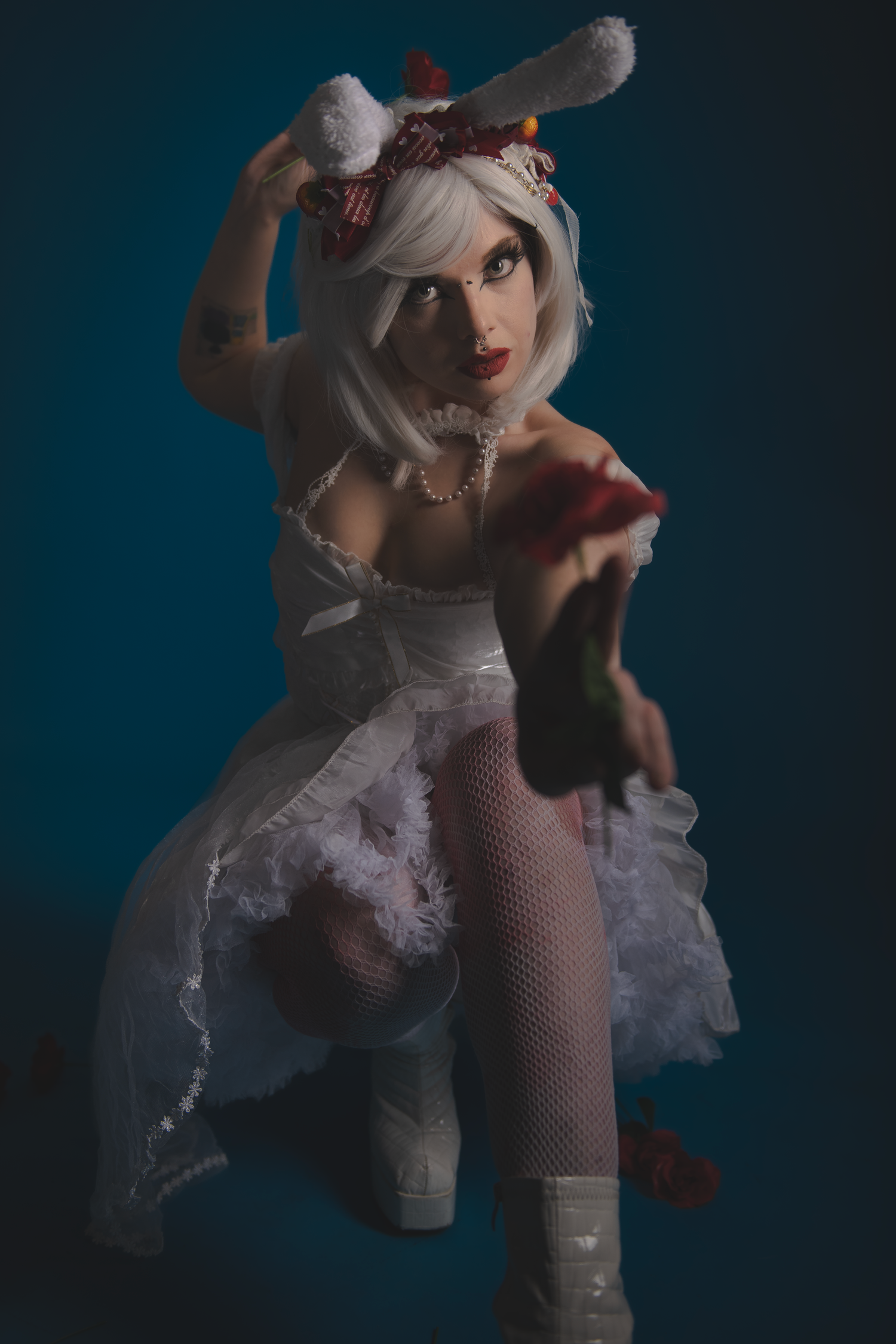Artistic boudoir photo showcasing white dress and bunny ears costume against deep blue backdrop.