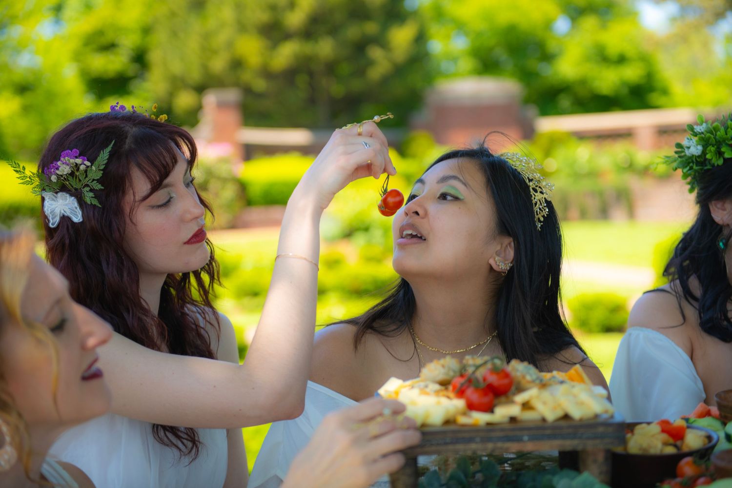 Friends share a playful moment while enjoying an outdoor picnic with fresh fruit on a sunny day in a garden setting.