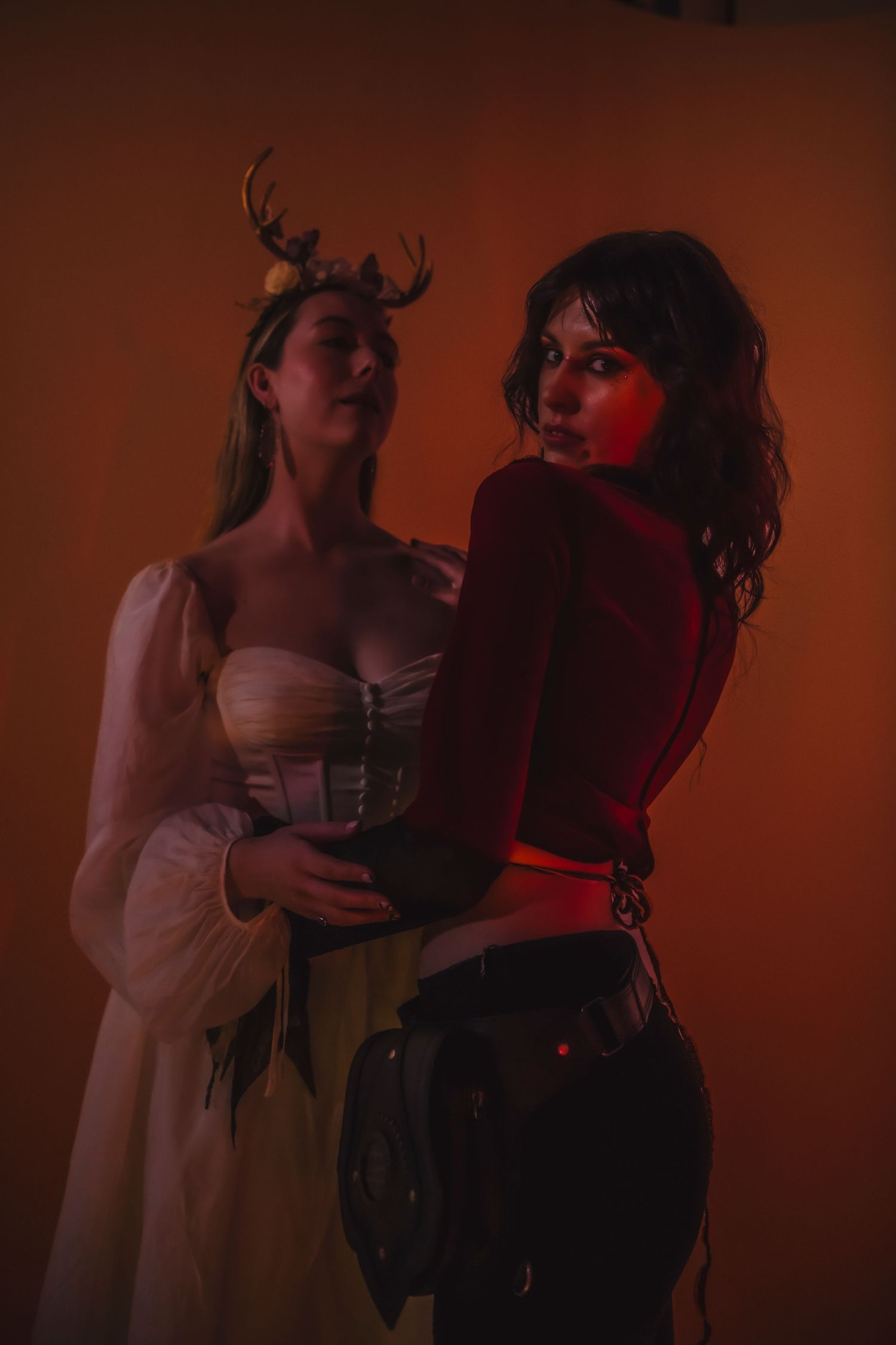 Two figures move expressively in a moody dark red-lit atmosphere during what appears to be a dramatic performance.