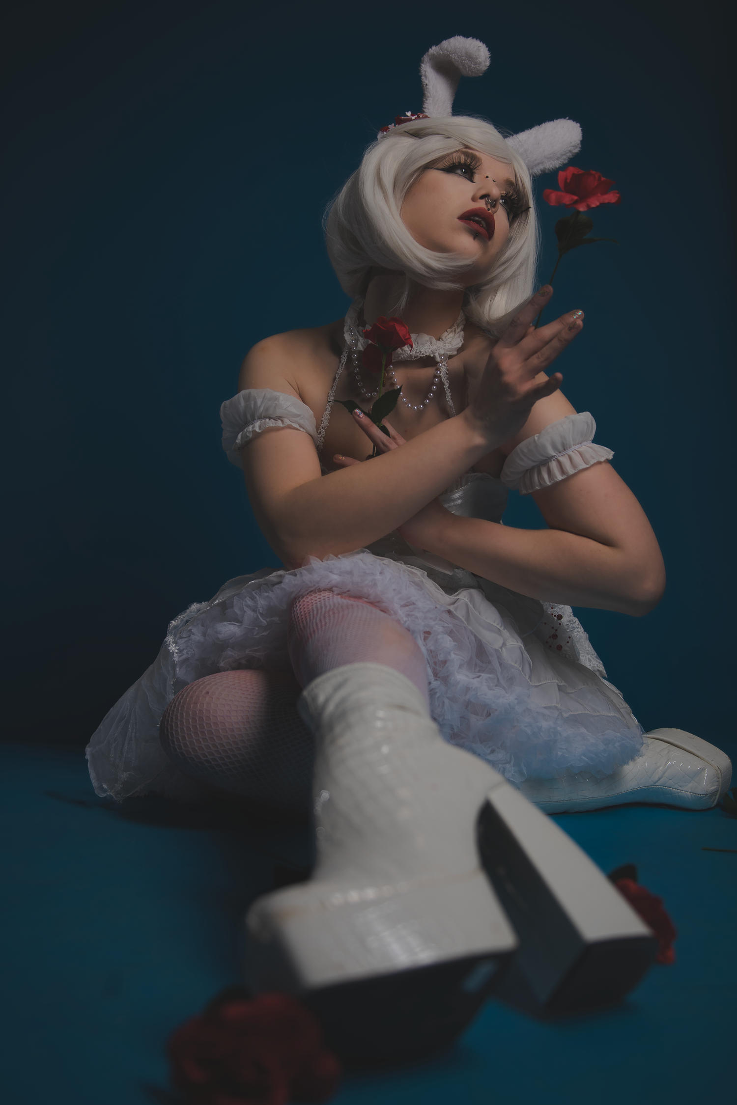 Fashion model in white dress and rabbit ears poses artistically against dark blue backdrop in dramatic studio photoshoot.