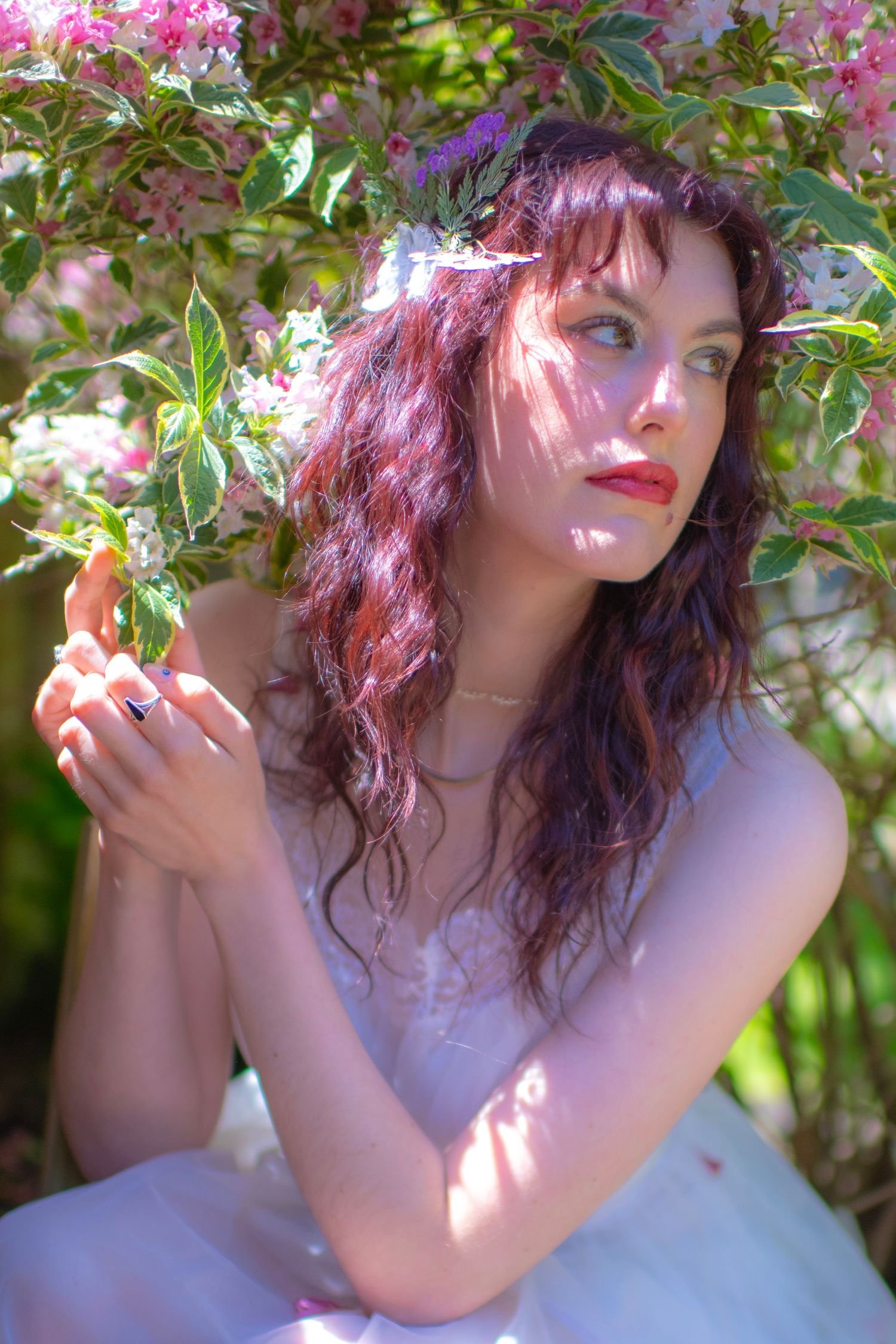 Ethereal spring portrait with pink blossoms and dappled sunlight filtering through green leaves in a garden setting.
