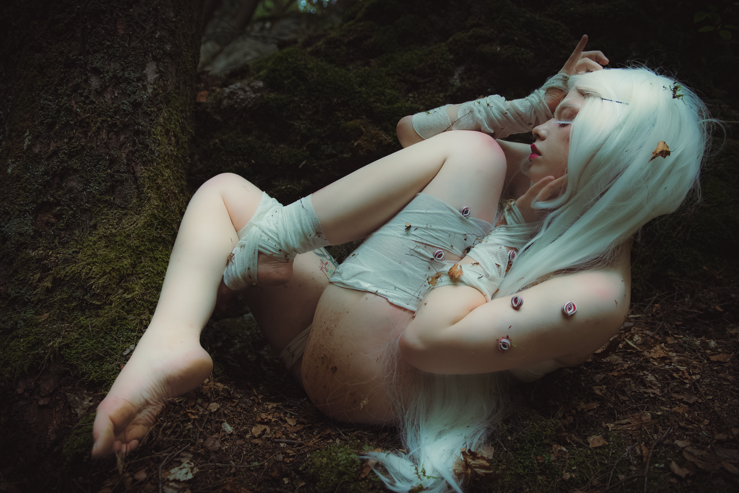 A person in a mint green dress lies gracefully on forest ground surrounded by fallen leaves and natural scenery.