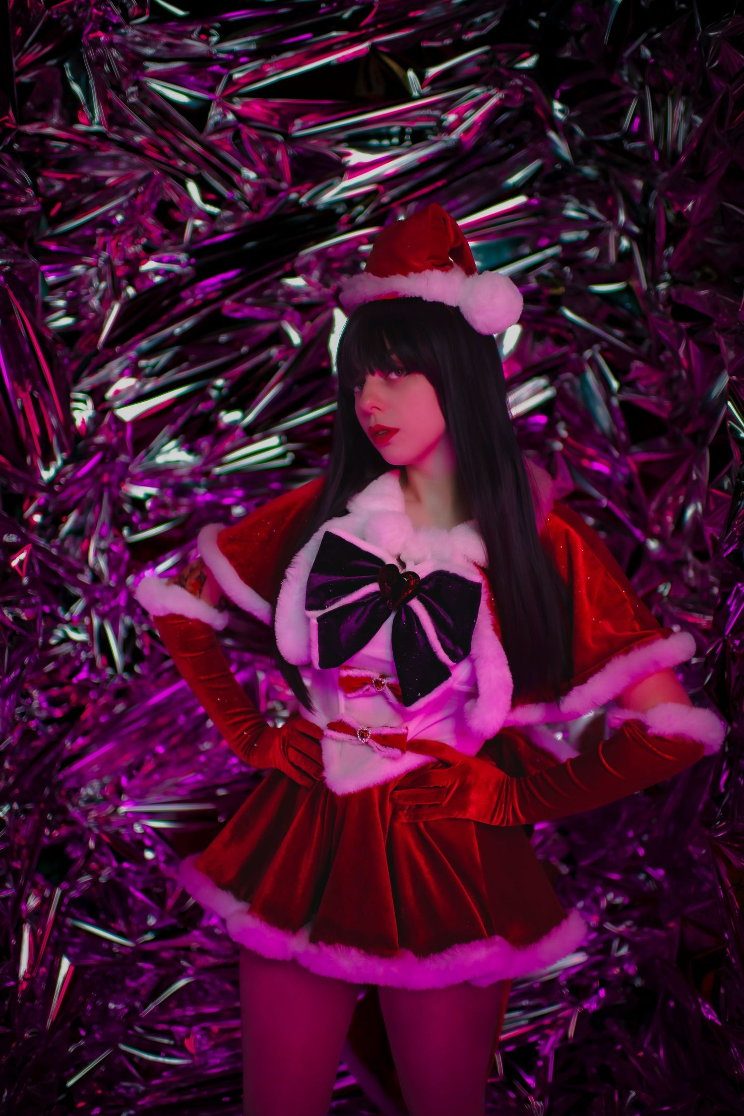 Figure in red velvet Santa dress poses against shimmering purple metallic background in dramatic lighting.
