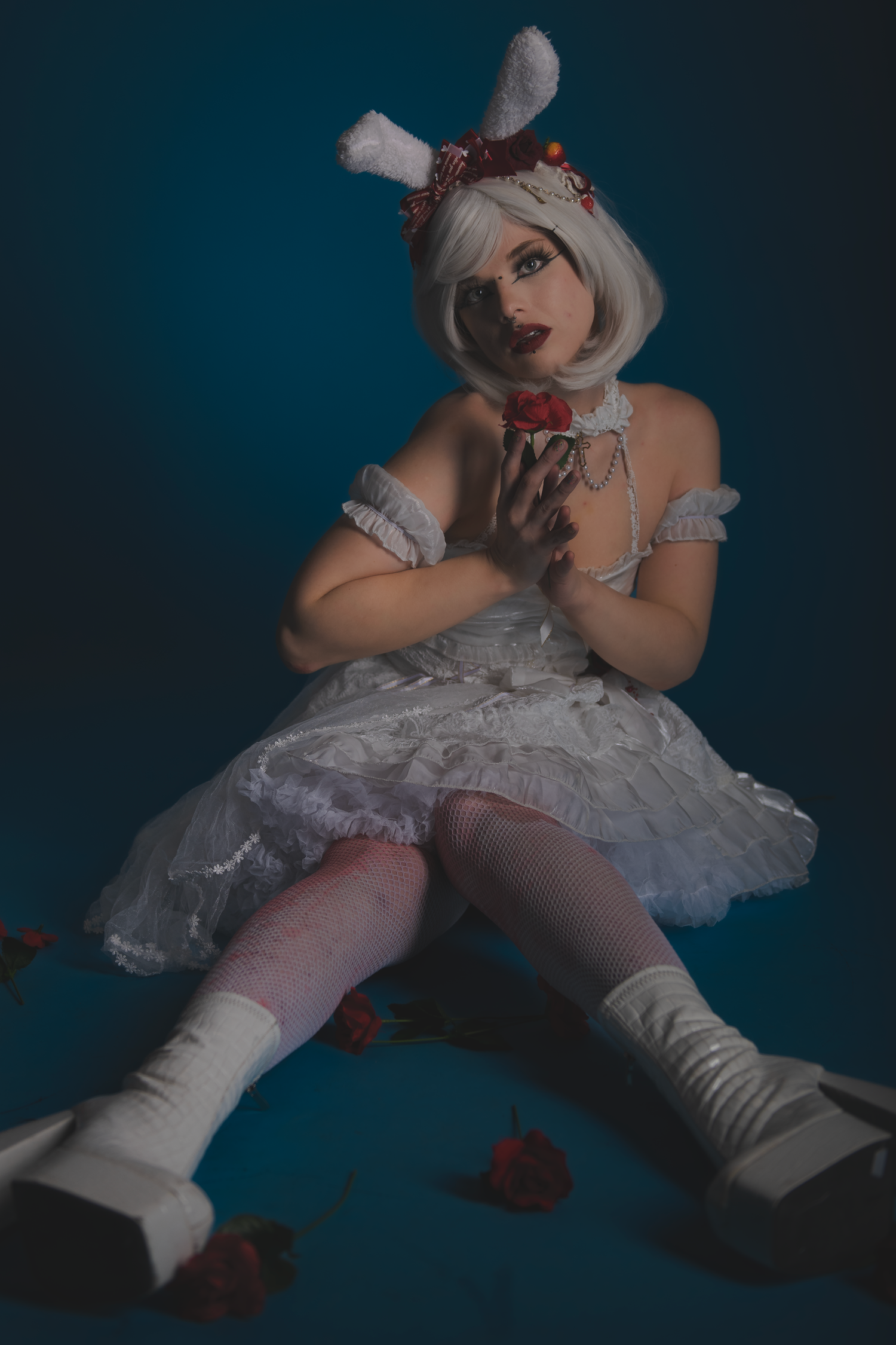 Model in white dress and stockings poses on floor in moody lighting with bunny ears.