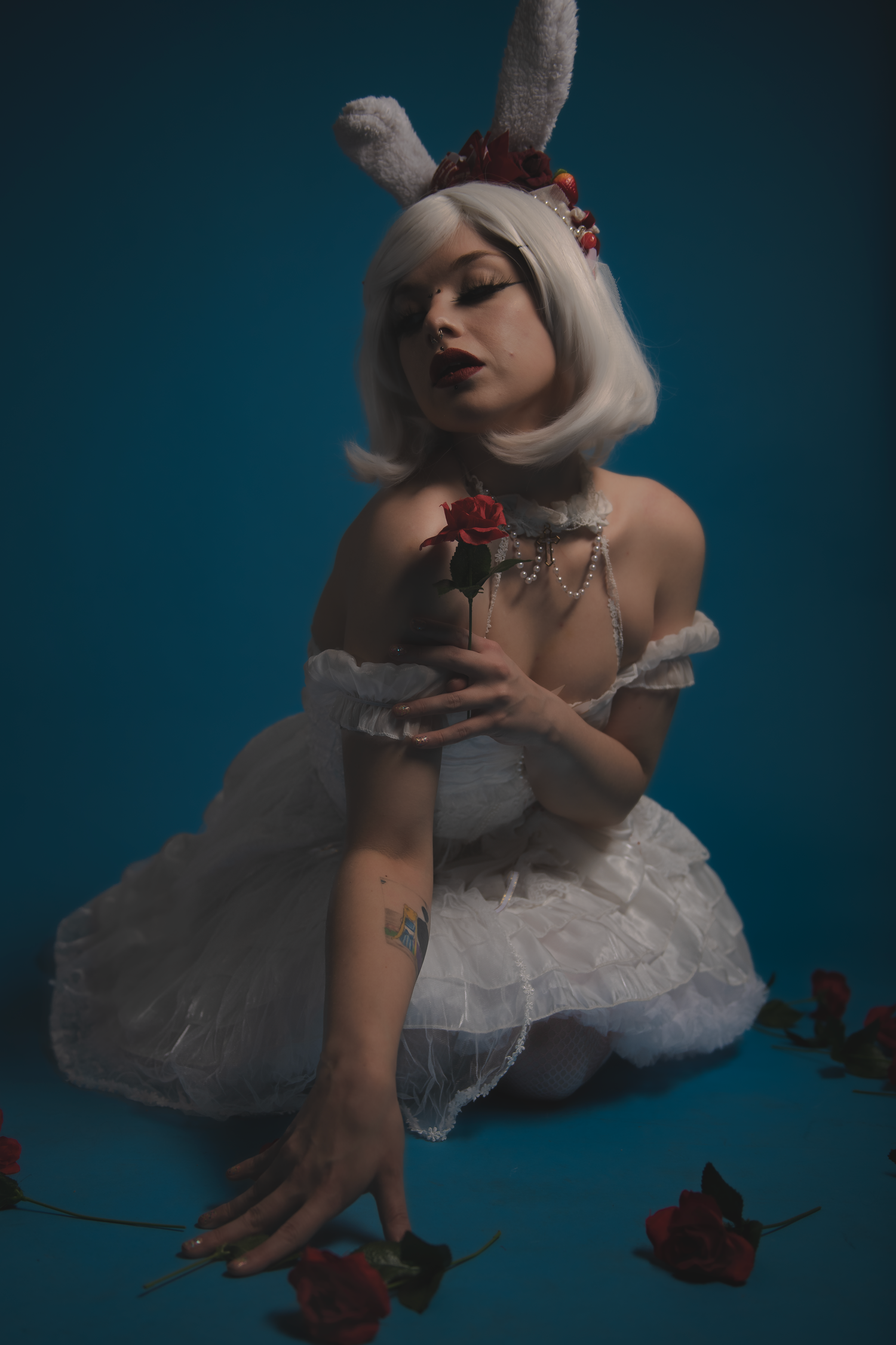 Artistic portrait featuring white bunny ears, tulle dress and red roses against a dark teal background in moody lighting.
