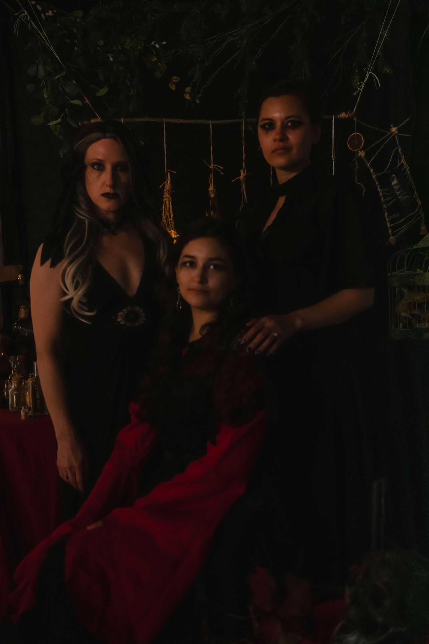 Romantic couple poses in dark garden setting wearing red dress and black clothing beside natural foliage at sunset.