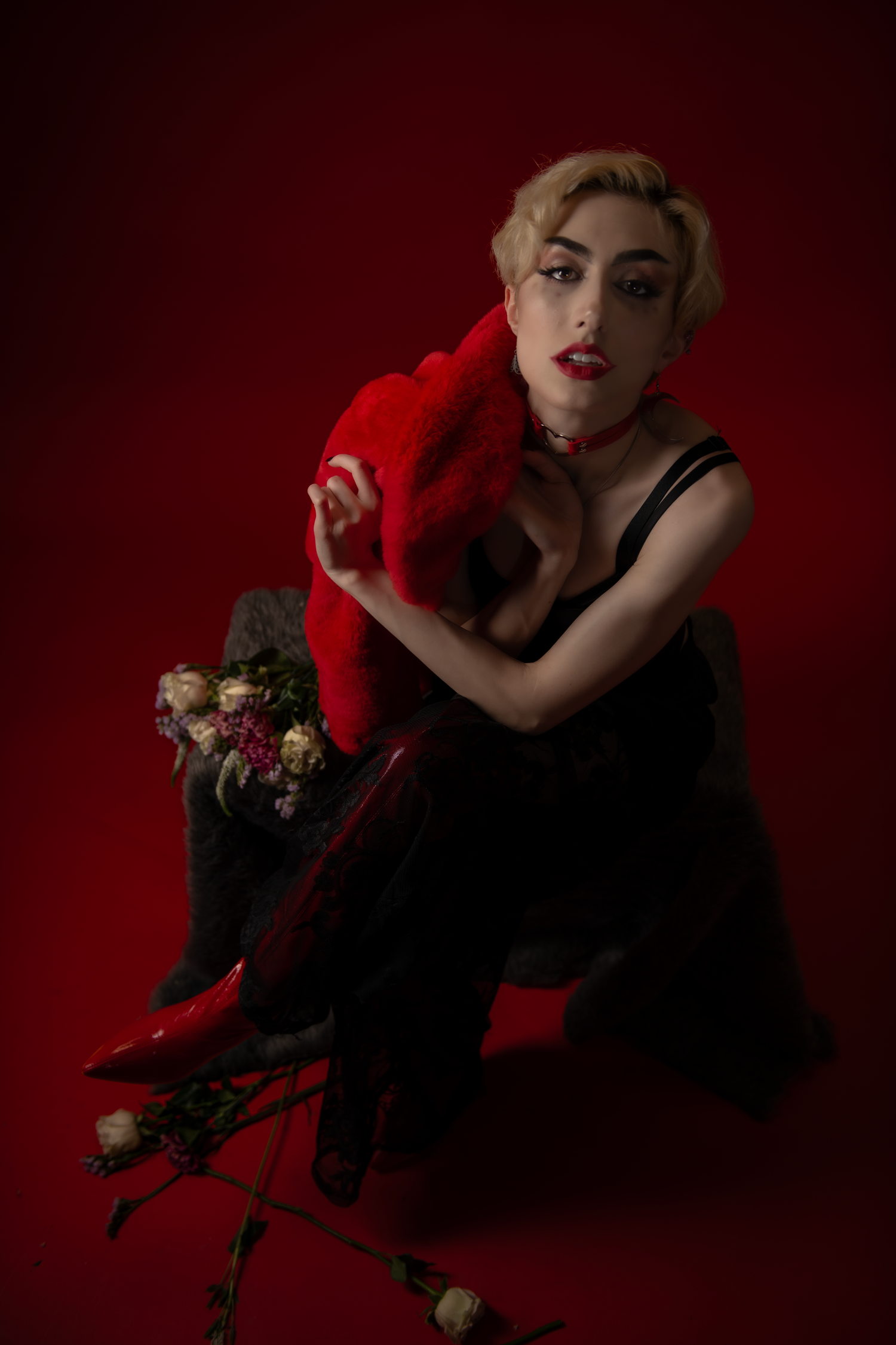 Dramatic portrait against red backdrop features vintage glamour styling with black dress, red accessories and floral accents.