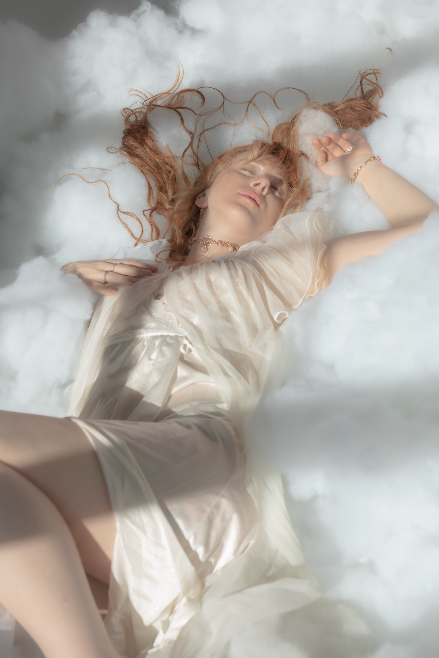 A dreamy ethereal photo series shows a figure in white reclining on clouds in an artistic composition.