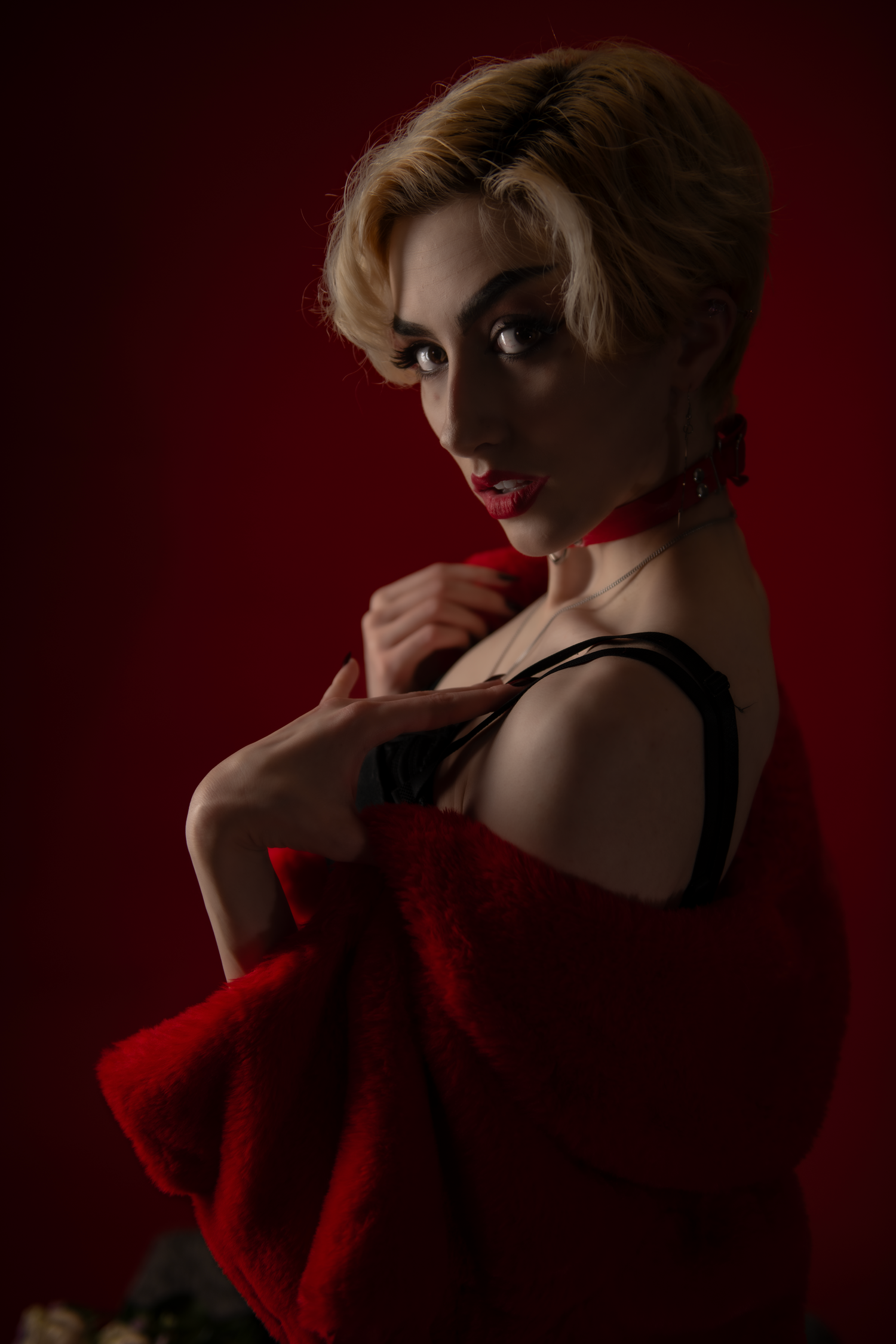 Dramatic portrait against dark red background featuring vintage style glamour with red fabric and black dress.
