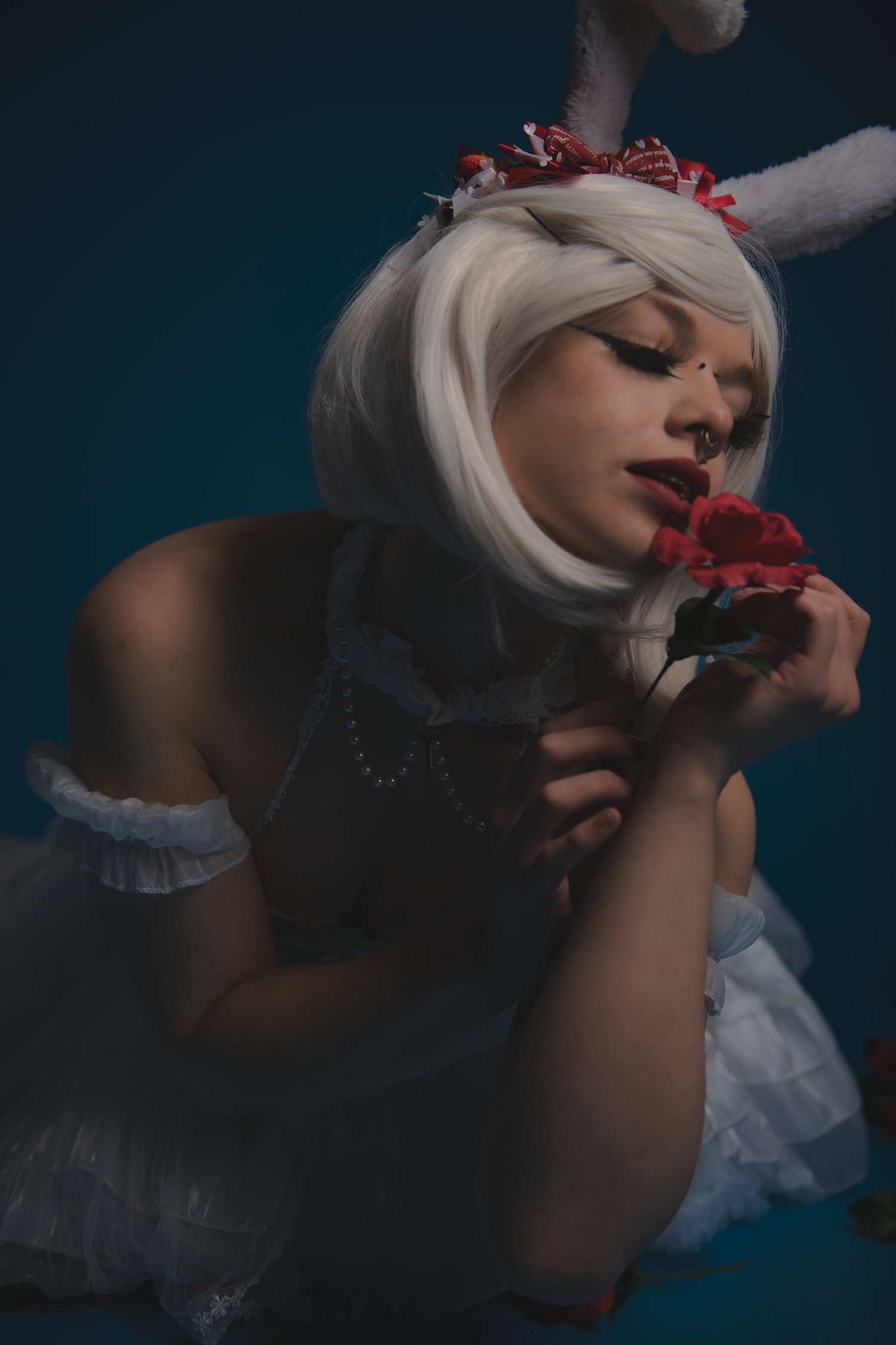 Moody fashion portrait with white hair and red roses in dark lighting creating dramatic gothic atmosphere.
