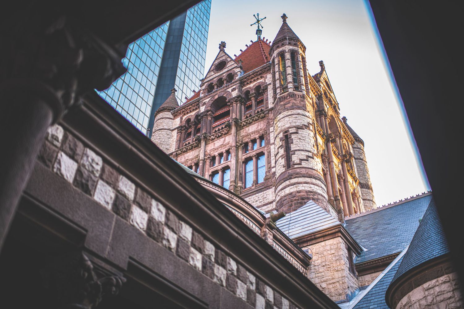 Gothic spires and ornate architectural details of a cathedral contrast against modern glass buildings in an urban setting.